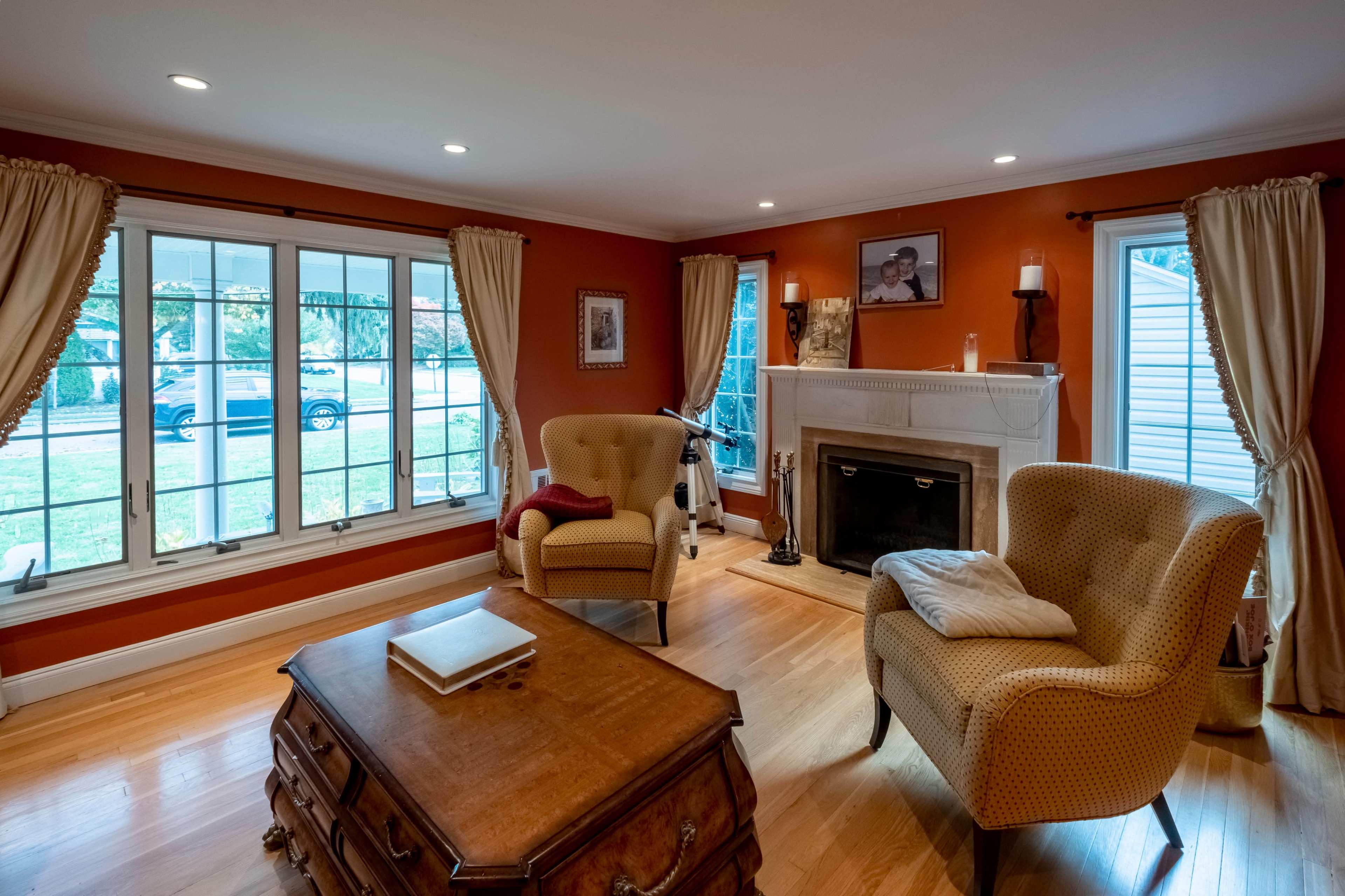 A living room features two armchairs, a coffee table, a fireplace, and large windows with views of the exterior.