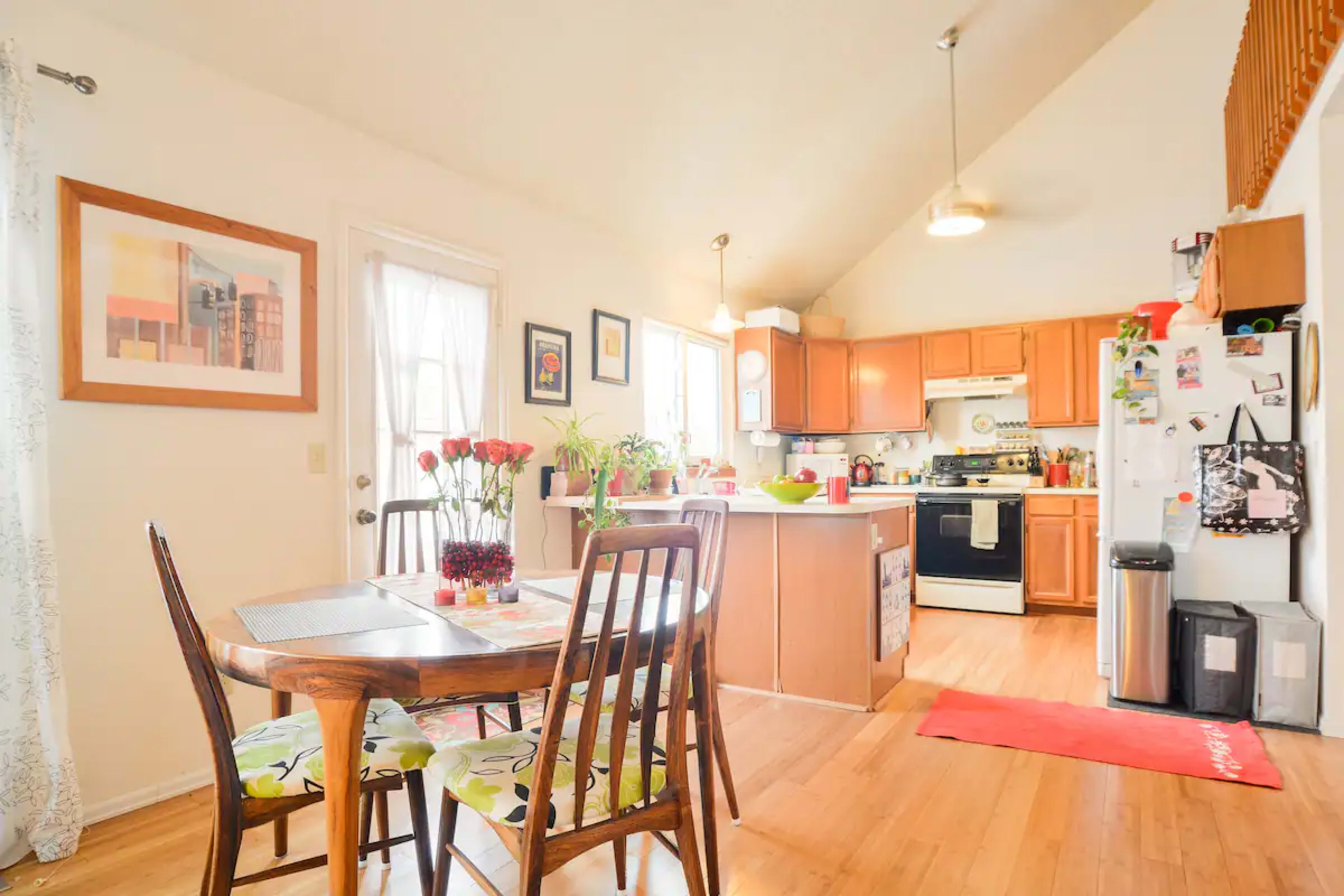 A bright kitchen features wooden cabinets, a dining table with four chairs, and a door leading outside.