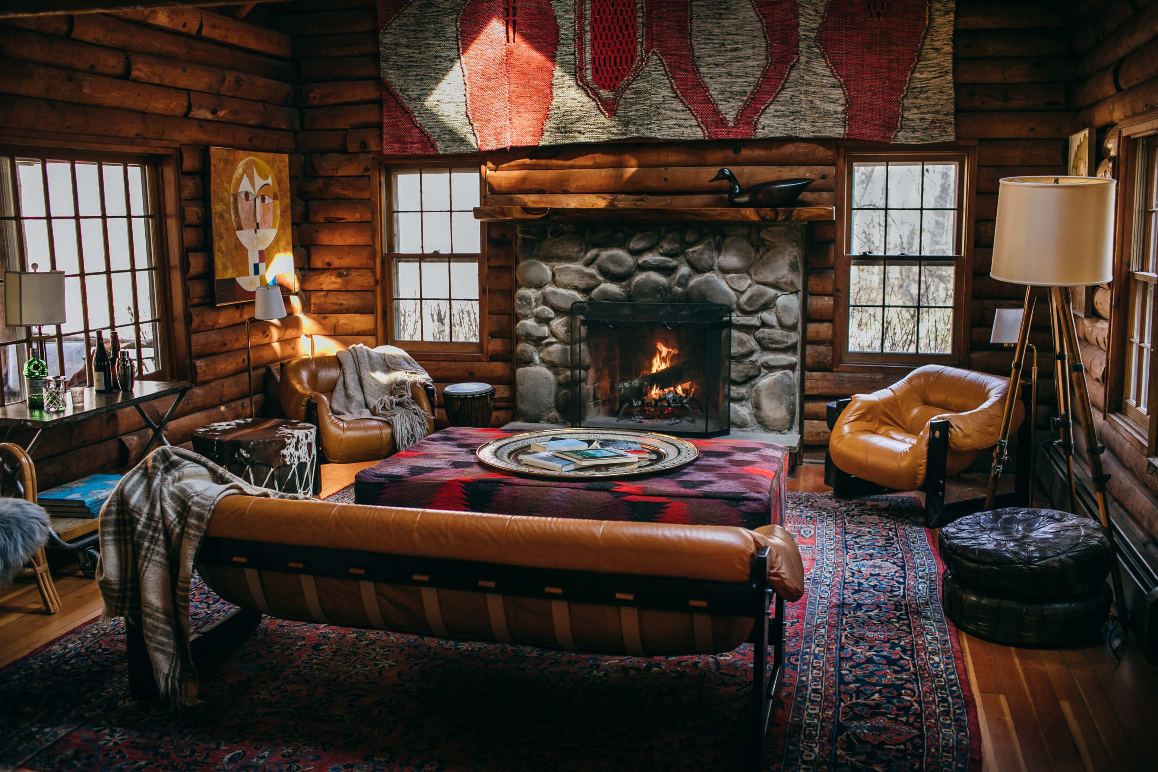 A cozy log cabin living room featuring a stone fireplace, a circular rug, and various seating arrangements.
