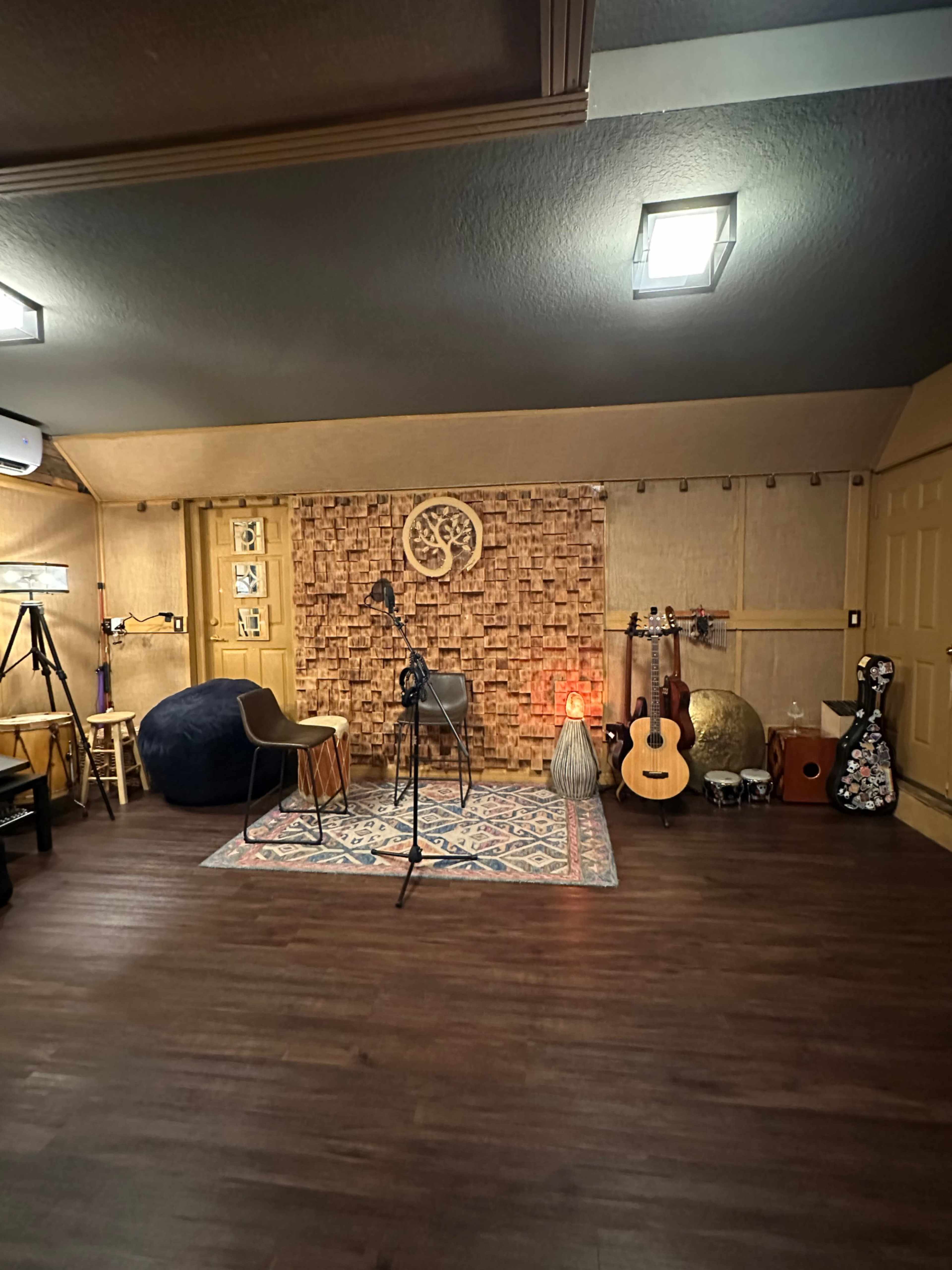A music recording studio featuring acoustic panels, microphones, chairs, and various musical instruments arranged in a warmly lit room.