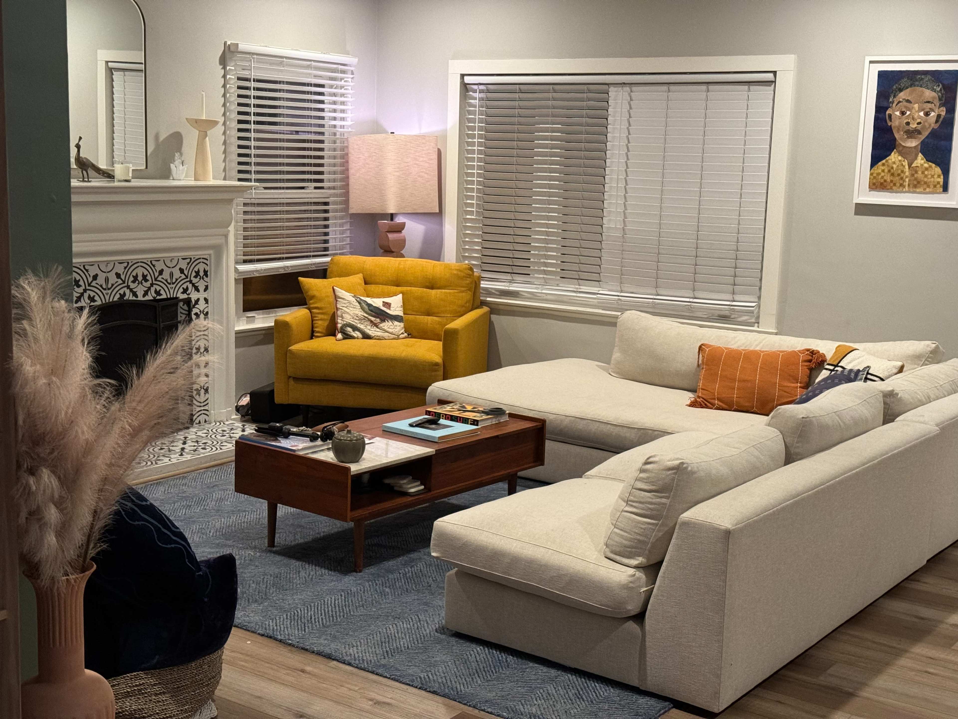 The scene shows a modern living room with a yellow armchair, a light-colored sectional sofa, a wooden coffee table, and a decorative fireplace.