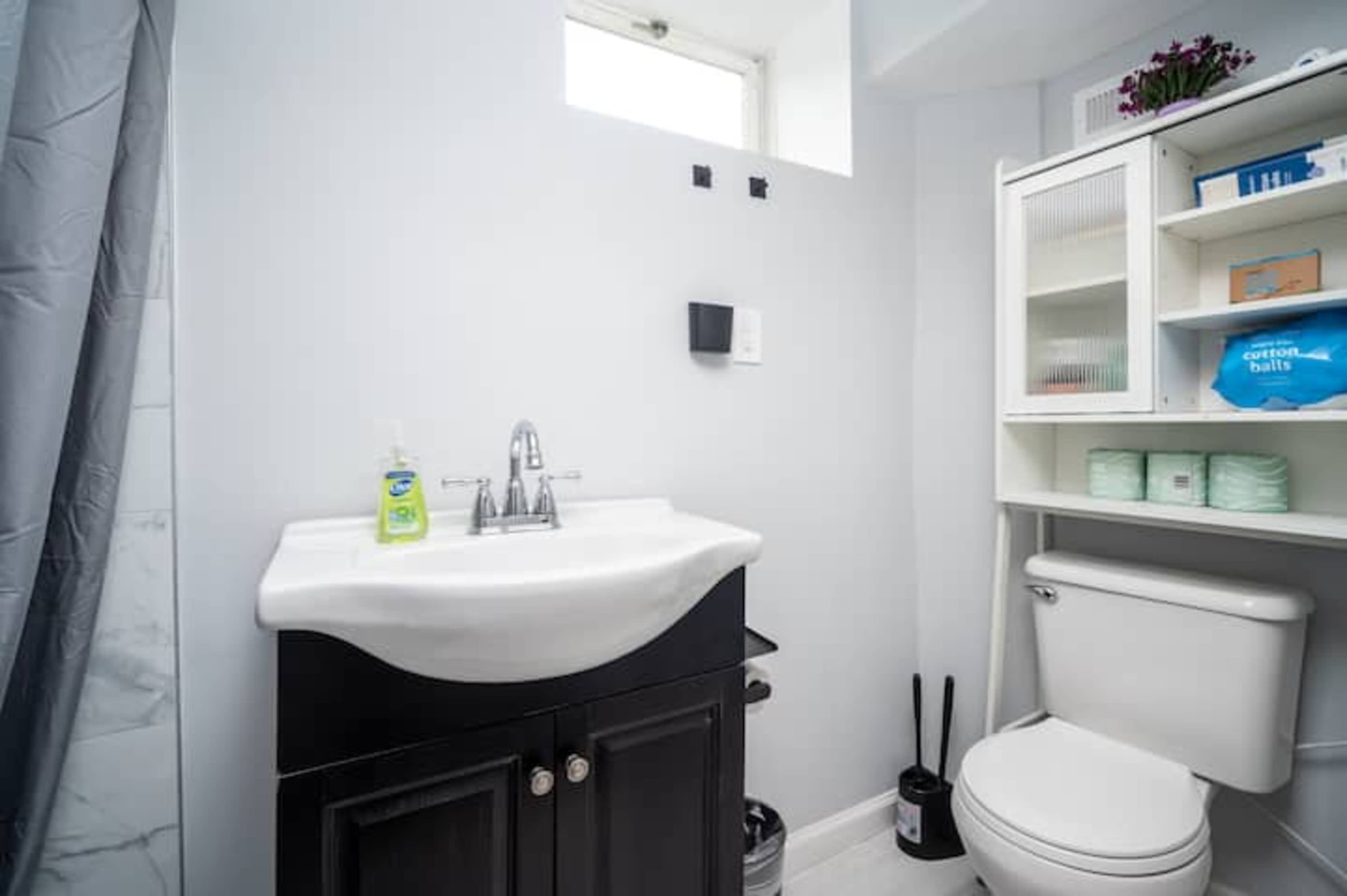 A bathroom featuring a white sink on a dark cabinet, a toilet, and a shelf with neatly arranged toiletries.