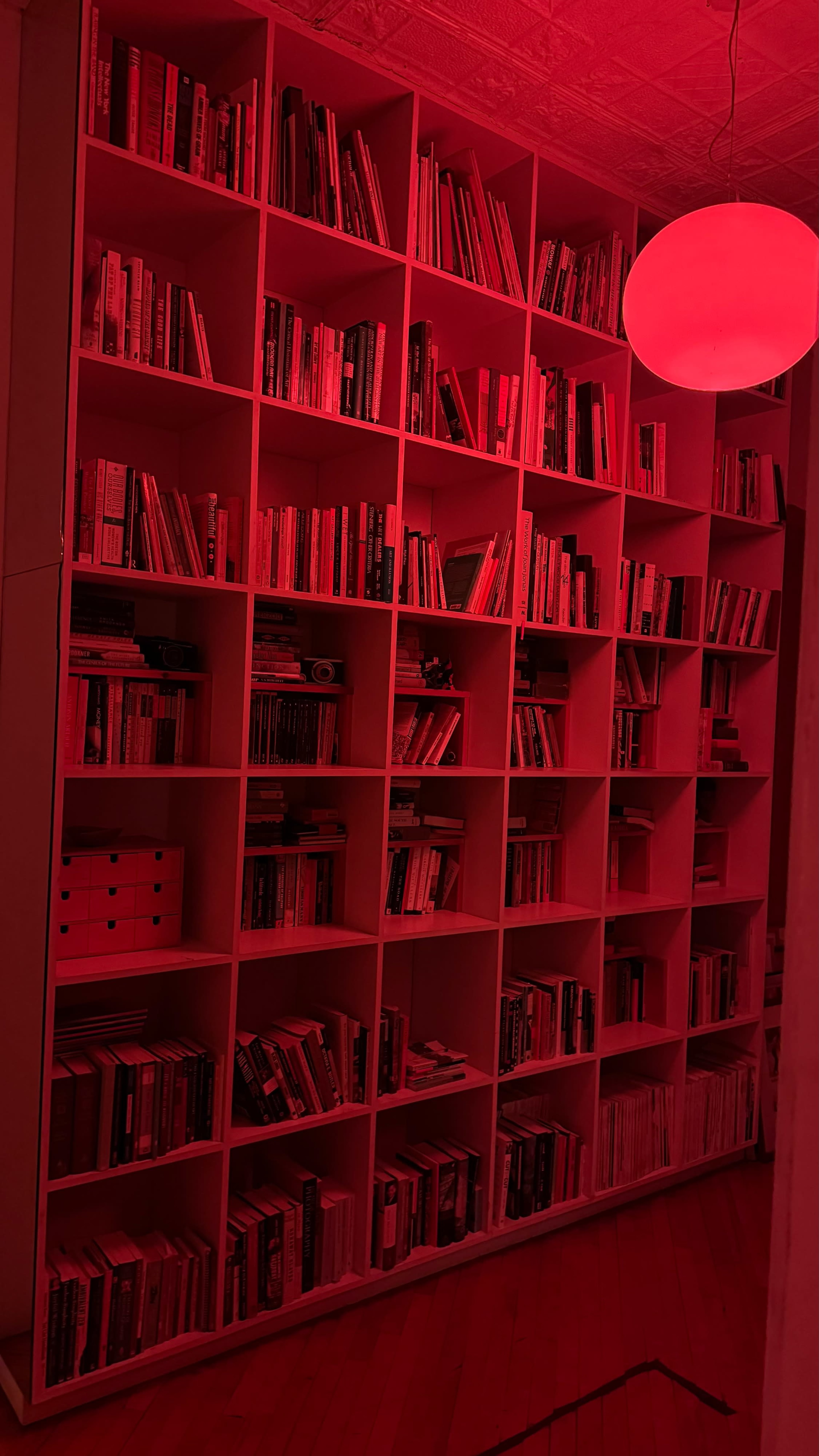 The image shows a bookshelf filled with various books, illuminated by a red light.