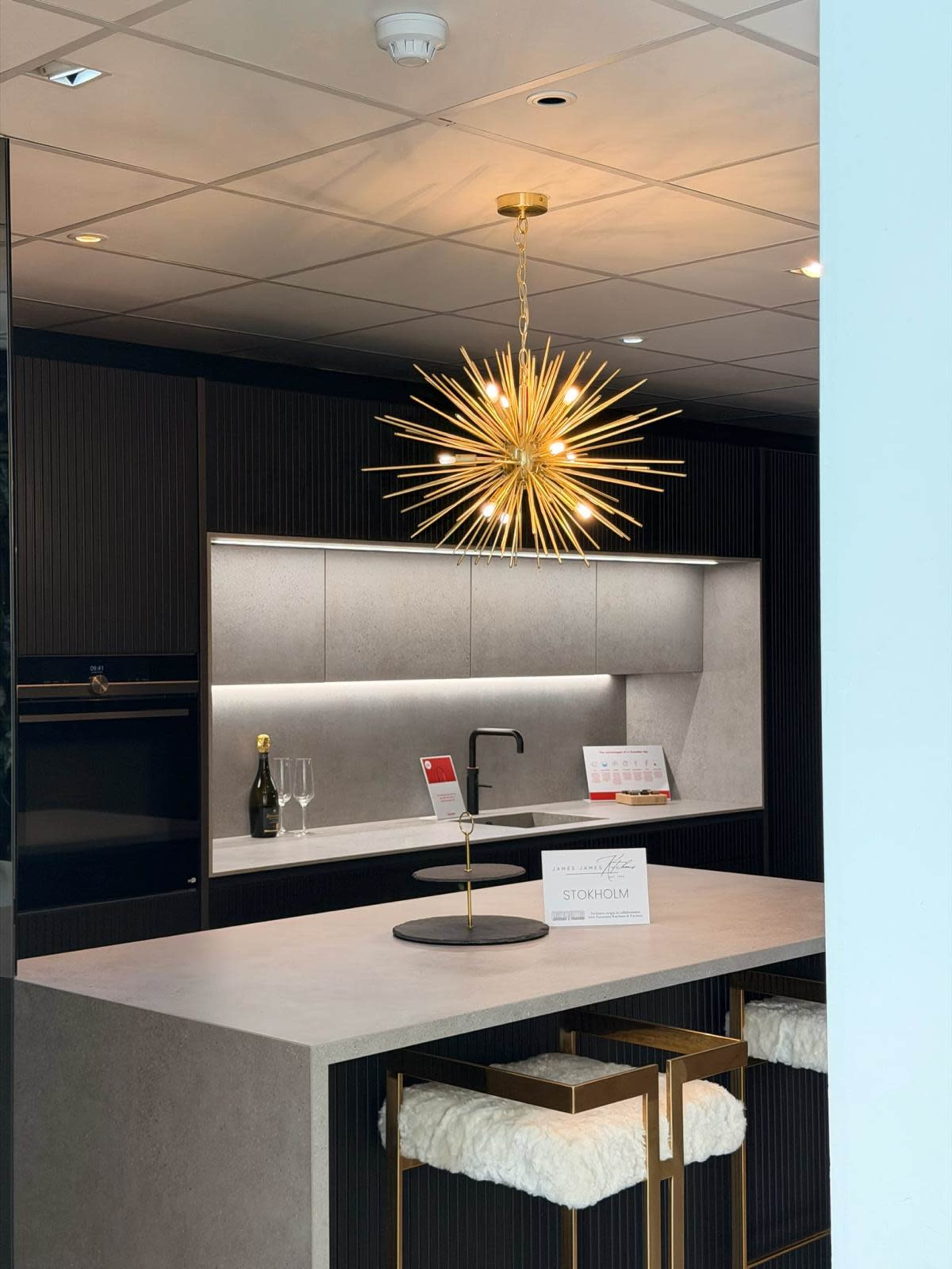 The image shows a modern kitchen featuring a starburst pendant light, a sleek countertop, and elegant bar stools.