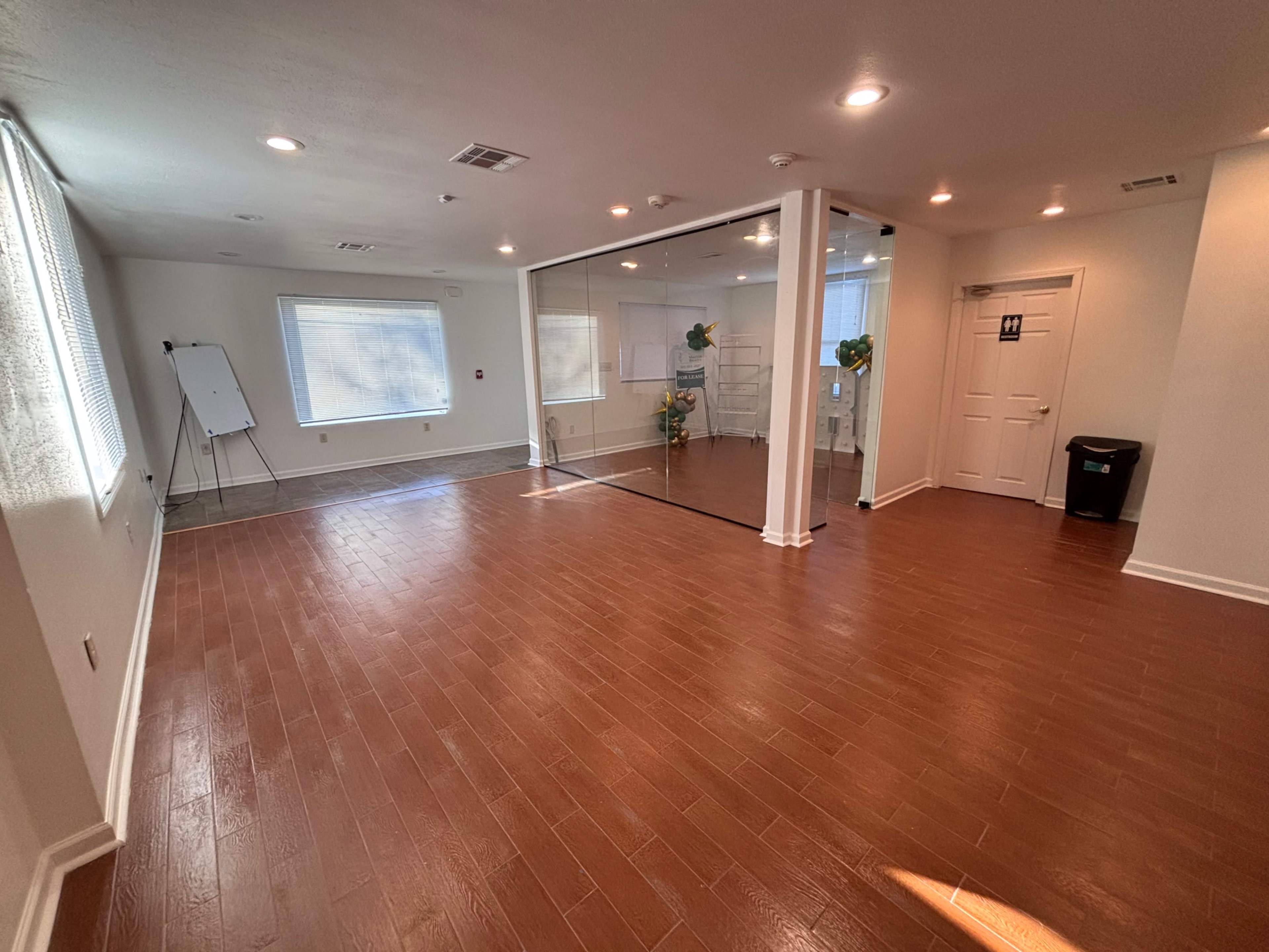 The spacious room features hardwood flooring, bright lighting, and a large mirrored wall, with a whiteboard and storage areas visible.