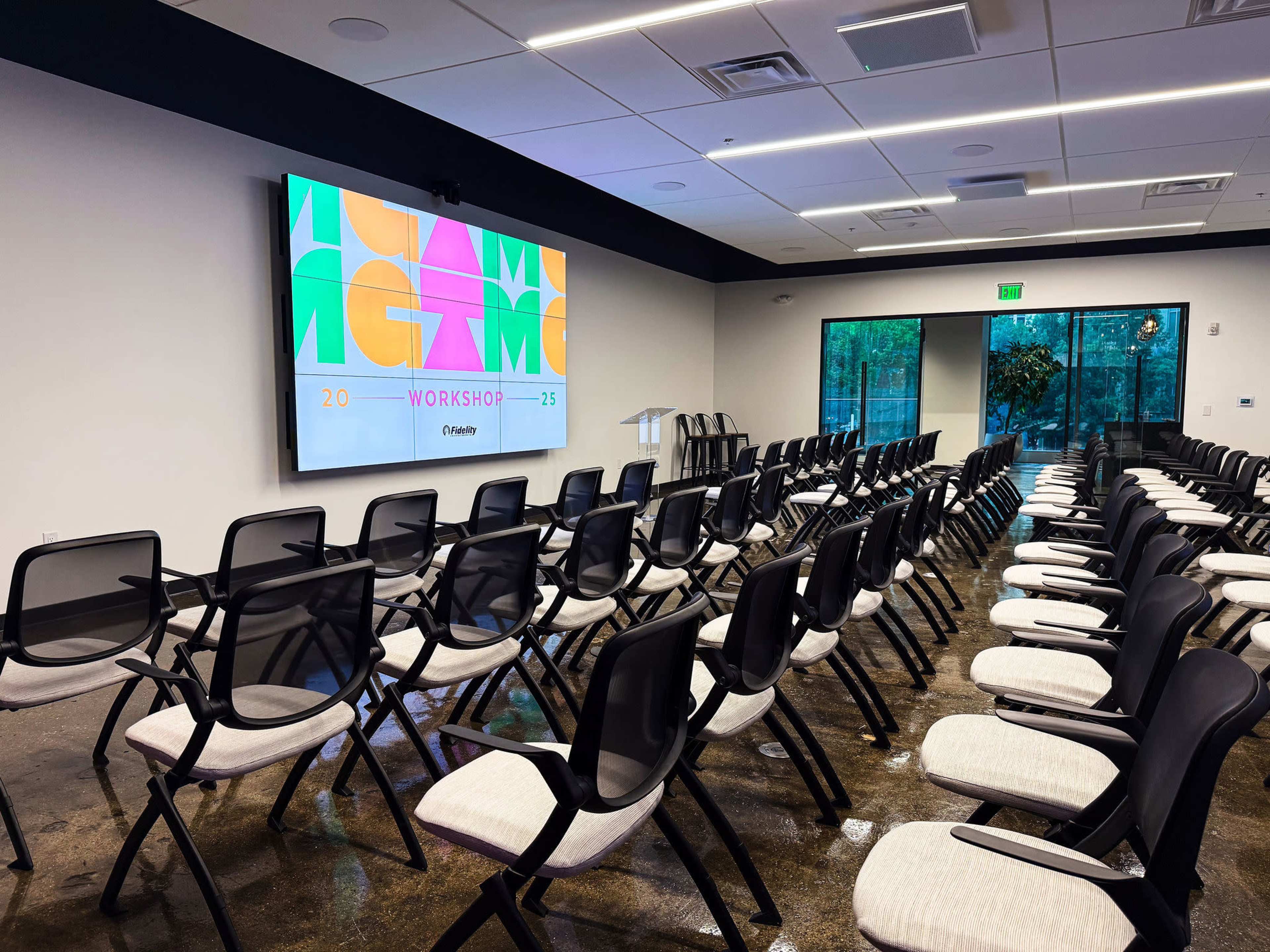 A workshop space is arranged with rows of black chairs facing a large screen displaying colorful graphics, ready for a presentation.