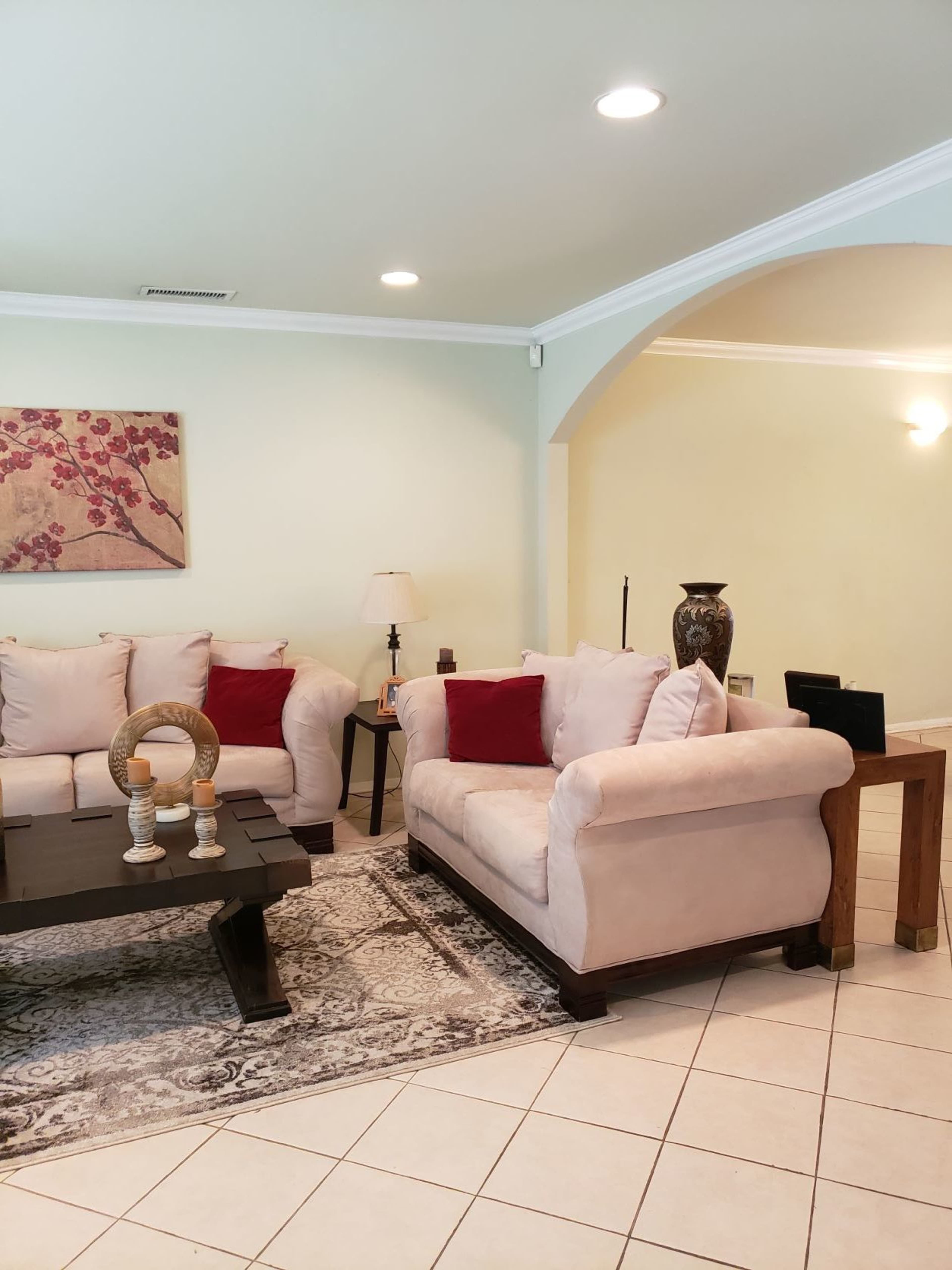 A living room with two beige sofas, a dark wooden coffee table, and a light-colored wall adorned with a floral artwork.