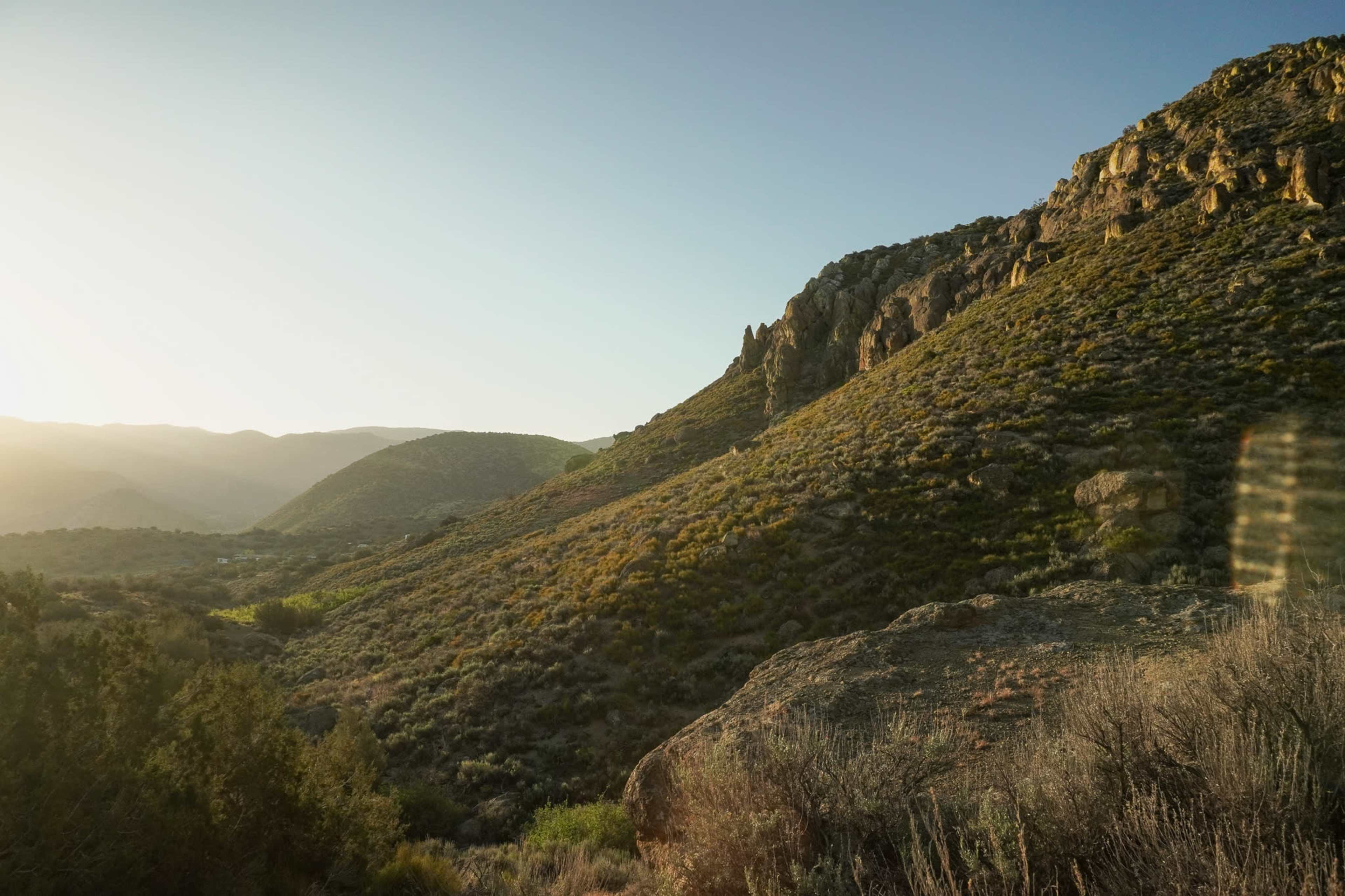 A hilly landscape with rocky outcrops and sparse vegetation under a clear sky.