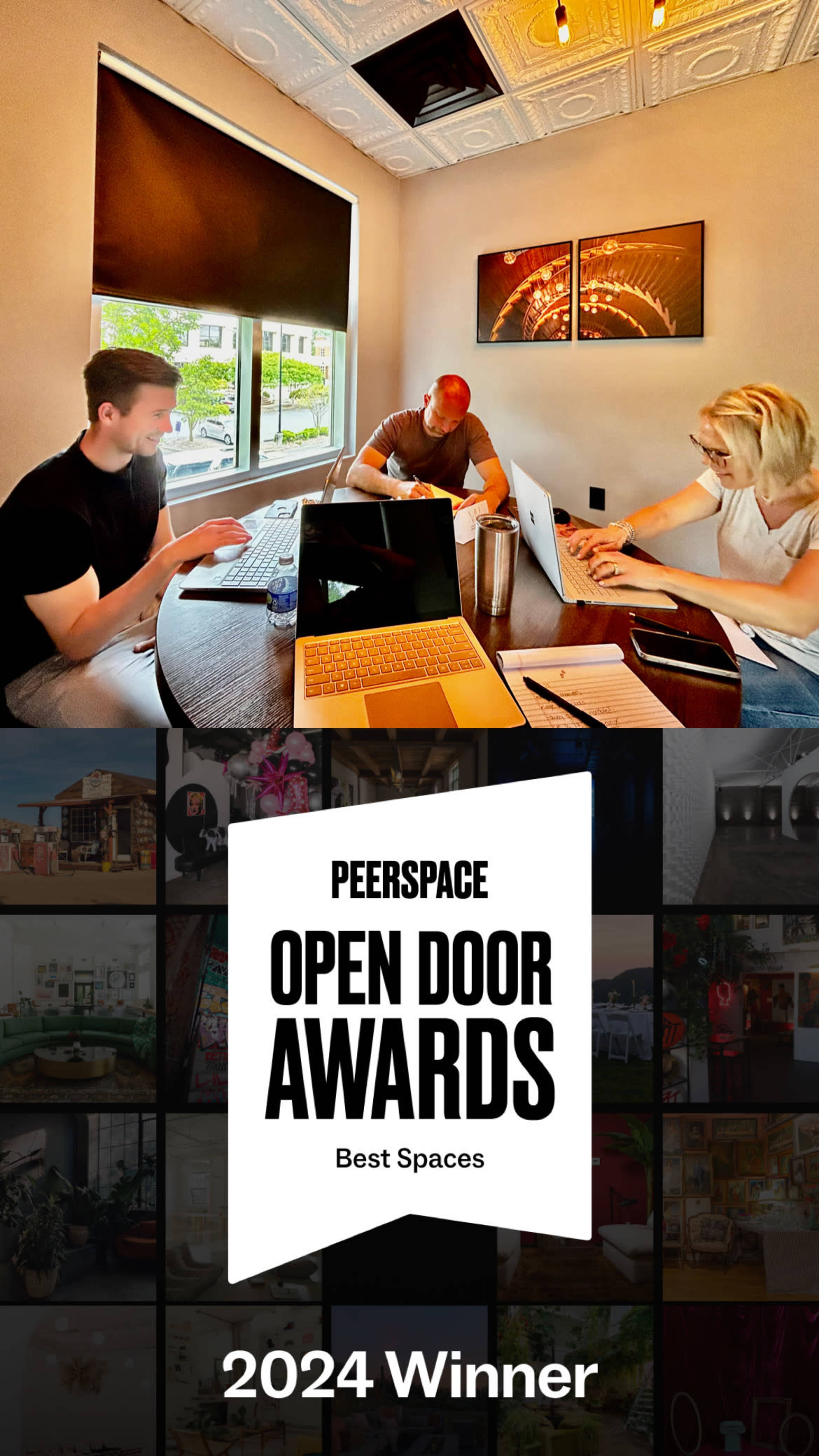 A group of three people is seated at a table with laptops and notebooks in a well-lit room featuring large windows.