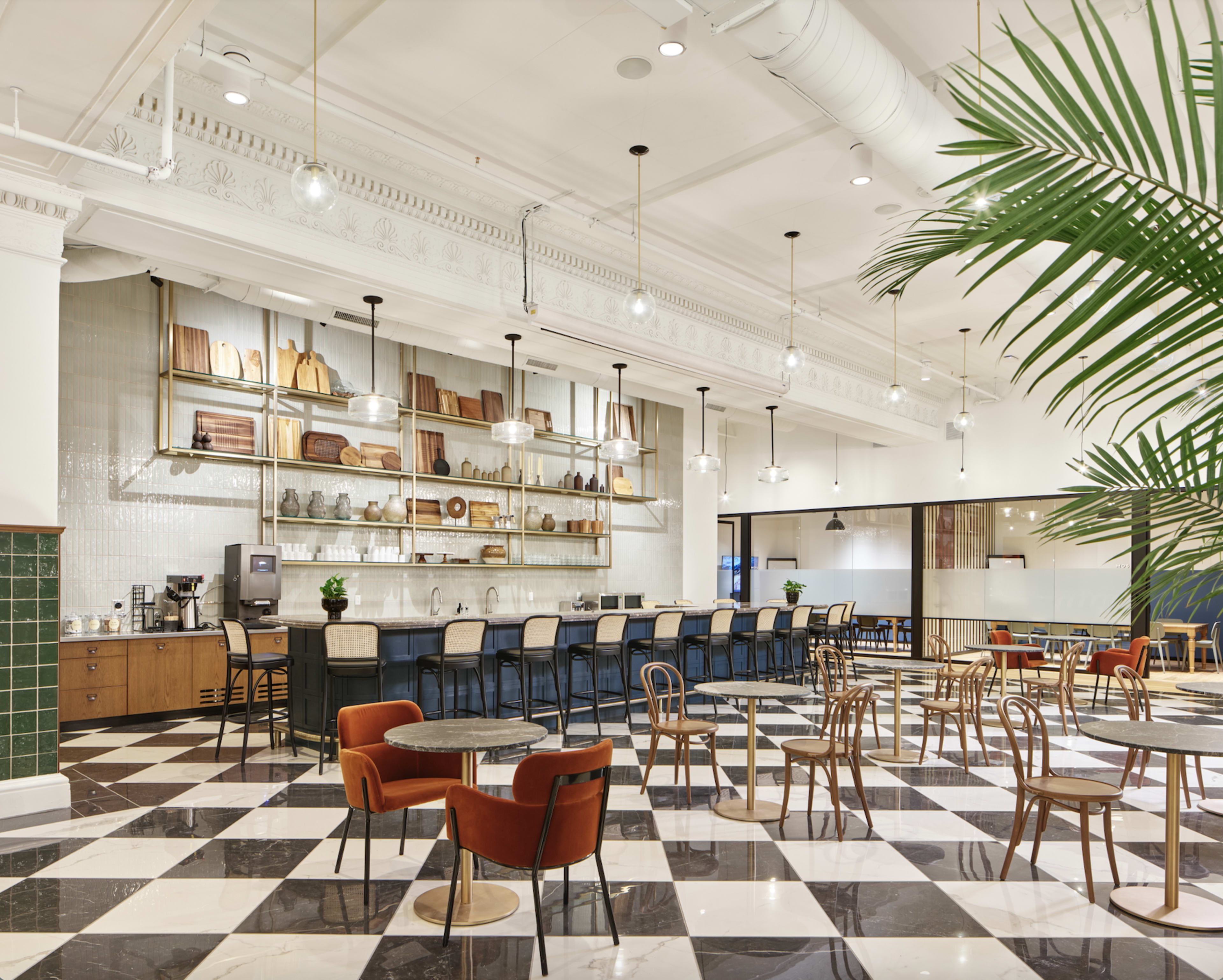 The image shows a spacious café interior with a checkerboard floor, shelves displaying wooden items, and a seating area featuring various chairs and tables.