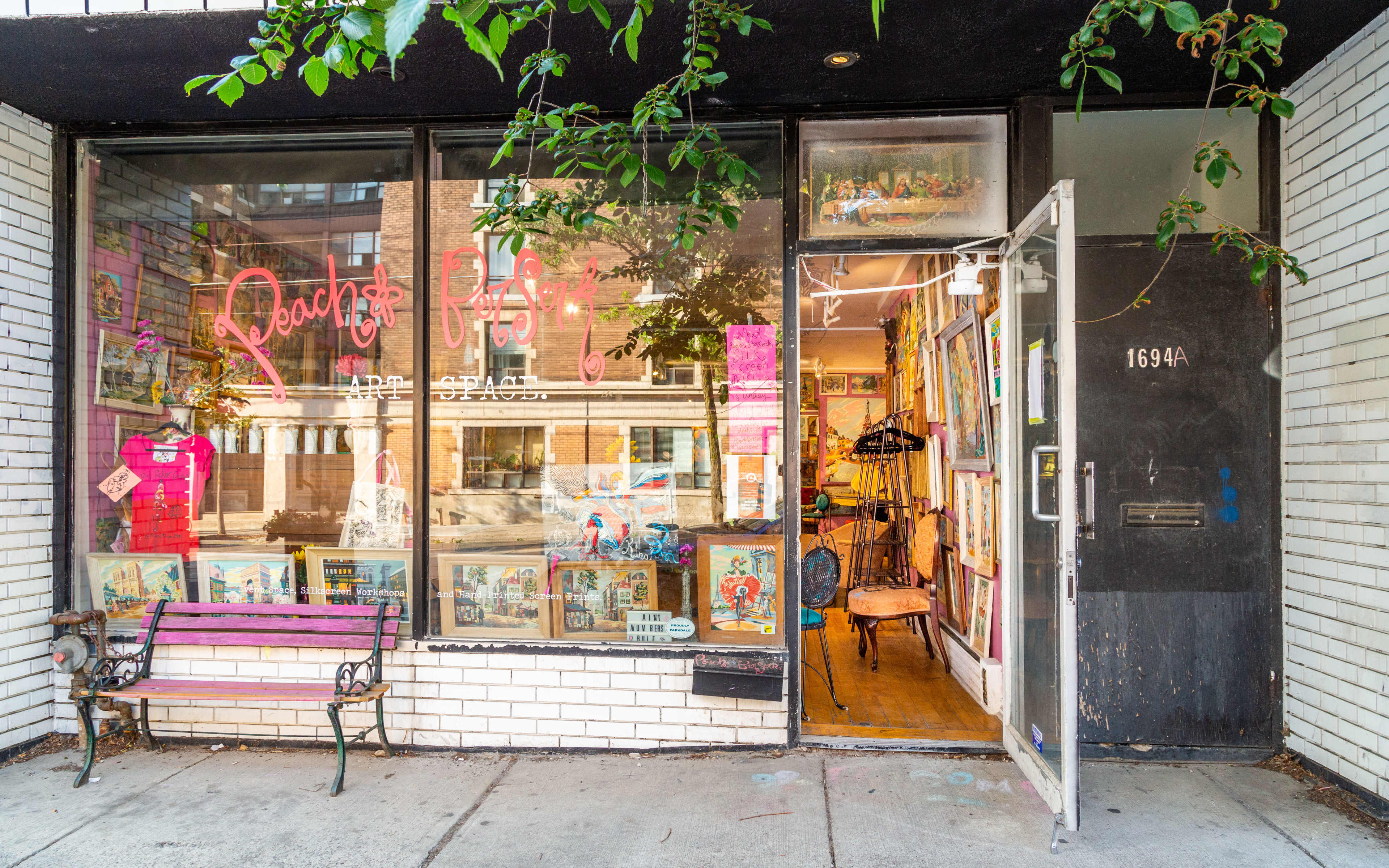 A storefront with a neon sign reading "Peach's Pyjamas" displays colorful artwork in the windows and an open door revealing a cozy interior.