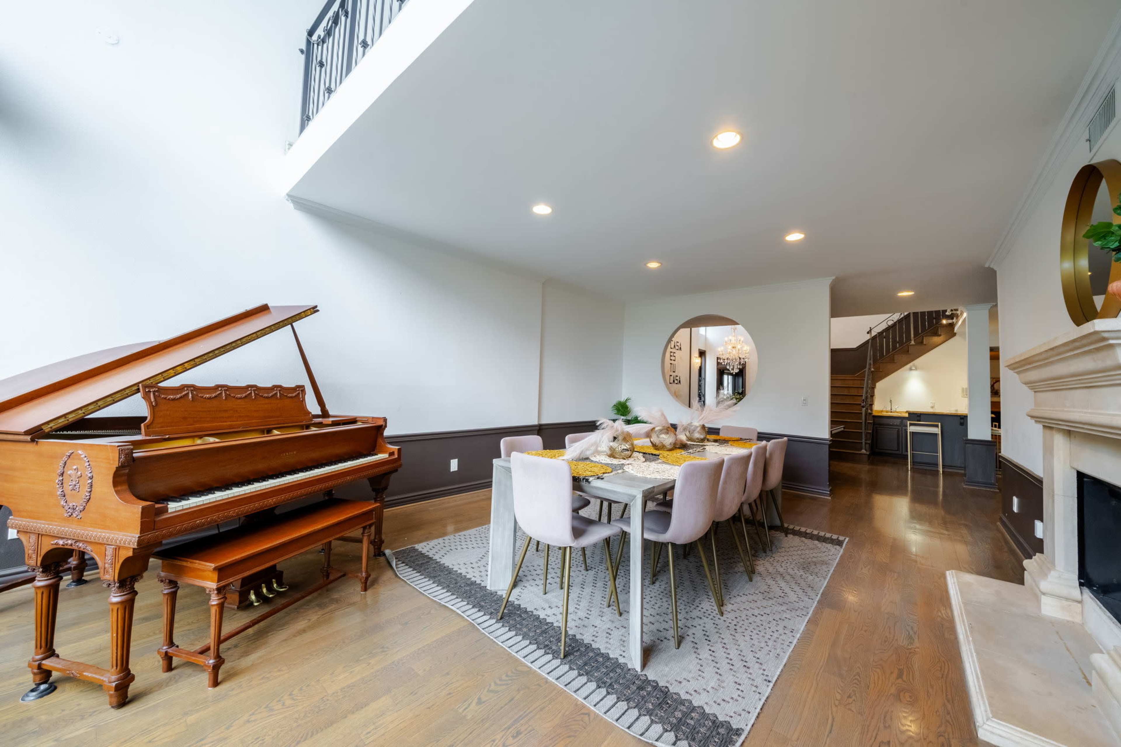 A spacious room featuring a grand piano on the left, a dining table set for multiple people in the center, and a staircase visible in the background.