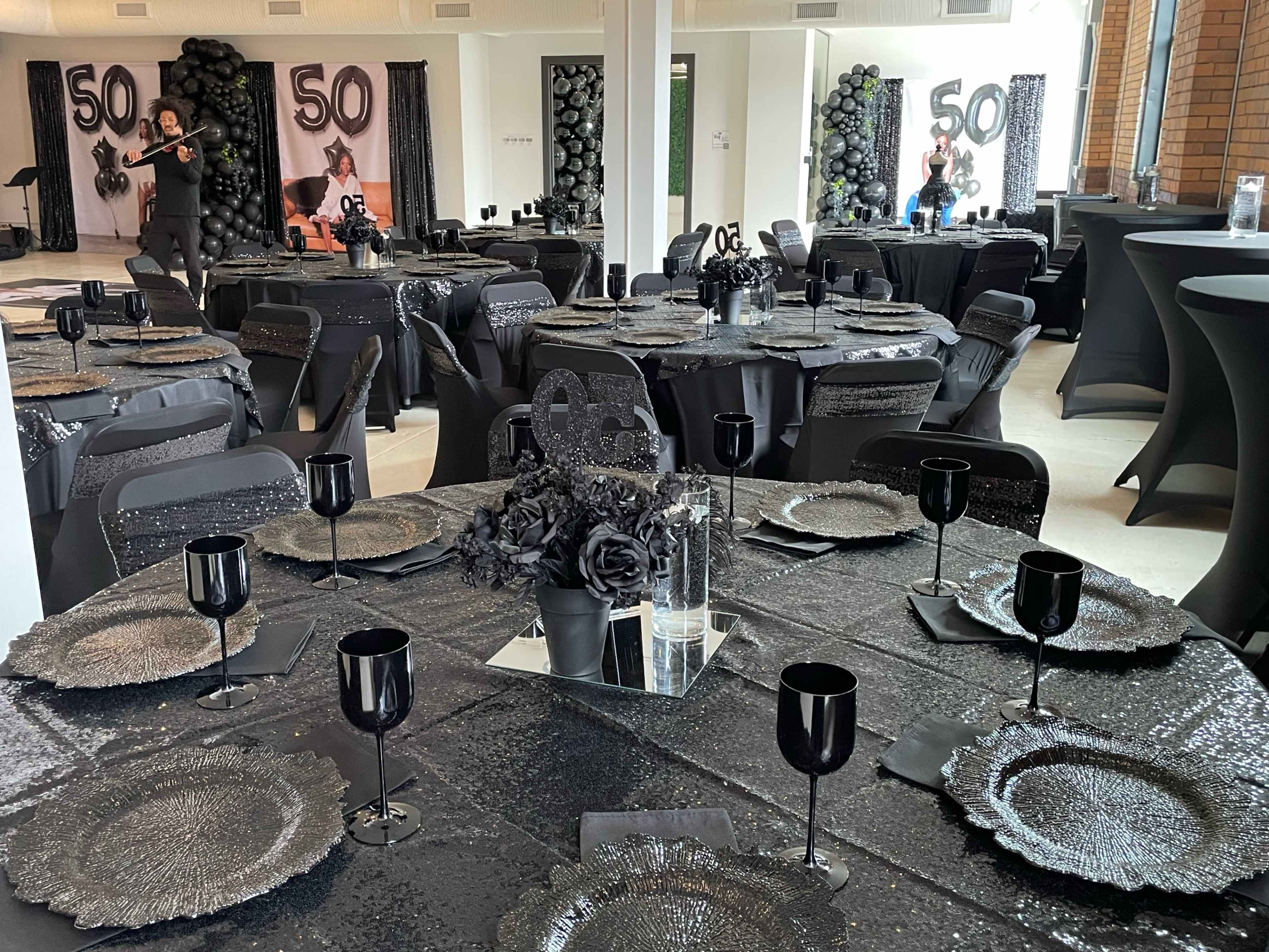 A decorated event space with black-themed tables and centerpieces, celebrating a 50th birthday.