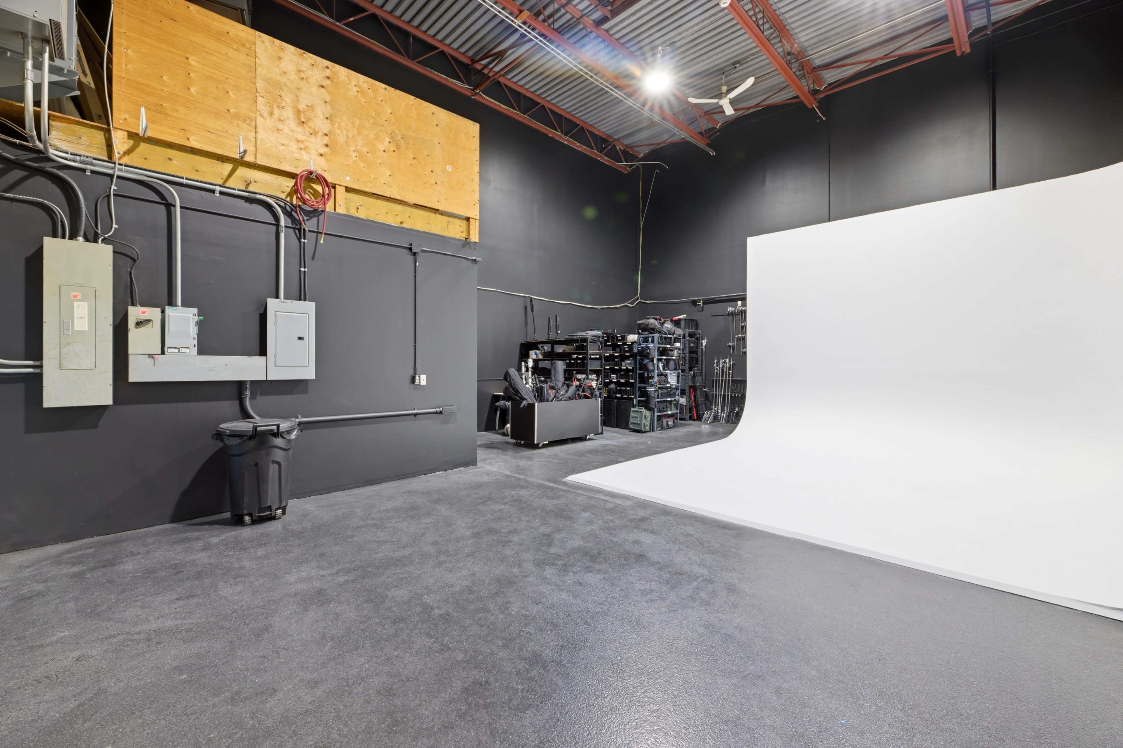 A photography studio features a white backdrop set against dark walls, with various equipment and storage units lining one side.