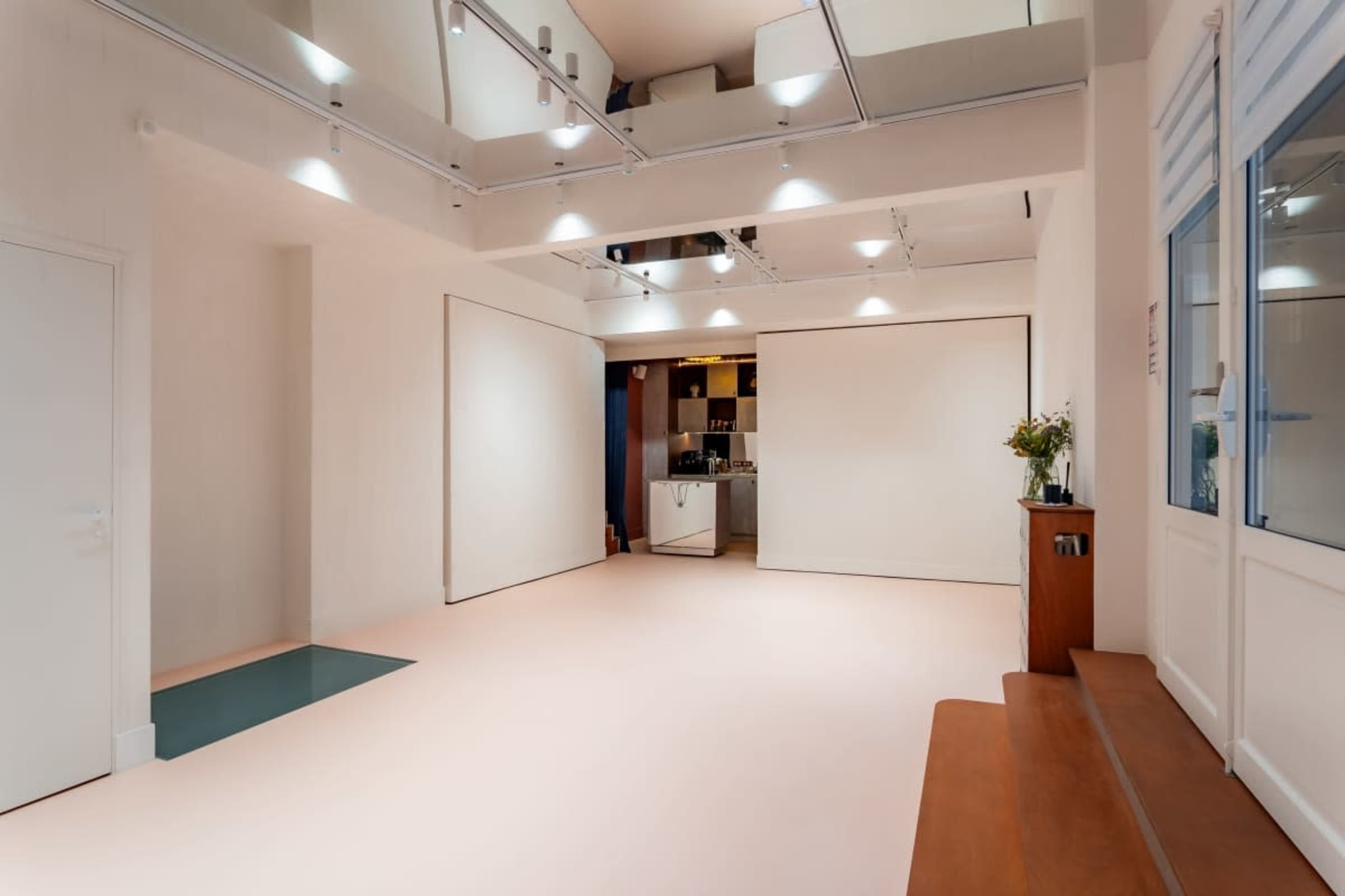 The image shows a spacious, well-lit interior with a minimalist design featuring light-colored walls and a combination of flooring surfaces.