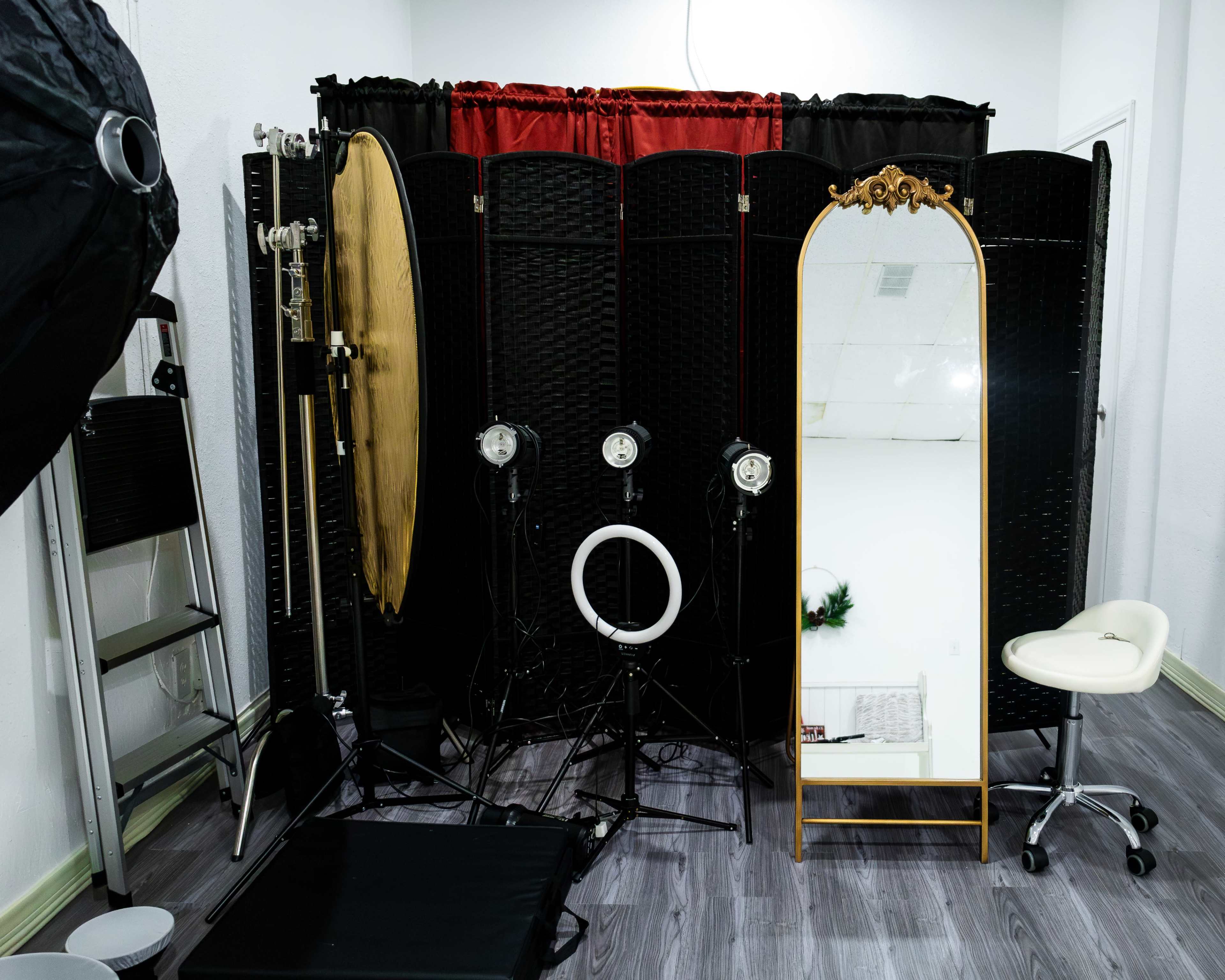 A photography studio setup featuring a large mirror, lighting equipment, and a privacy screen.