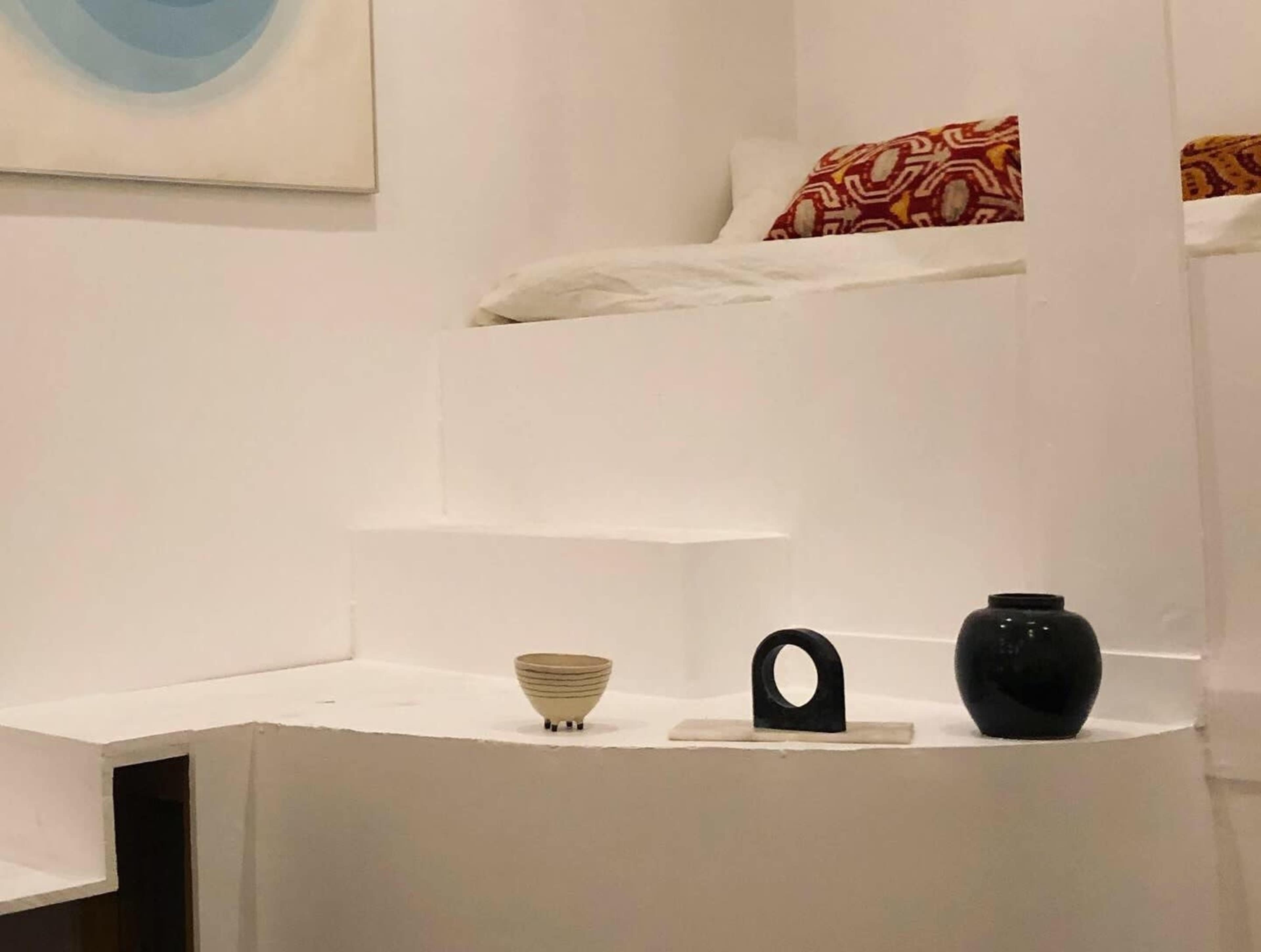 A minimalist interior space featuring a small staircase leading to a raised bedding area, with decorative items placed on a white surface below.