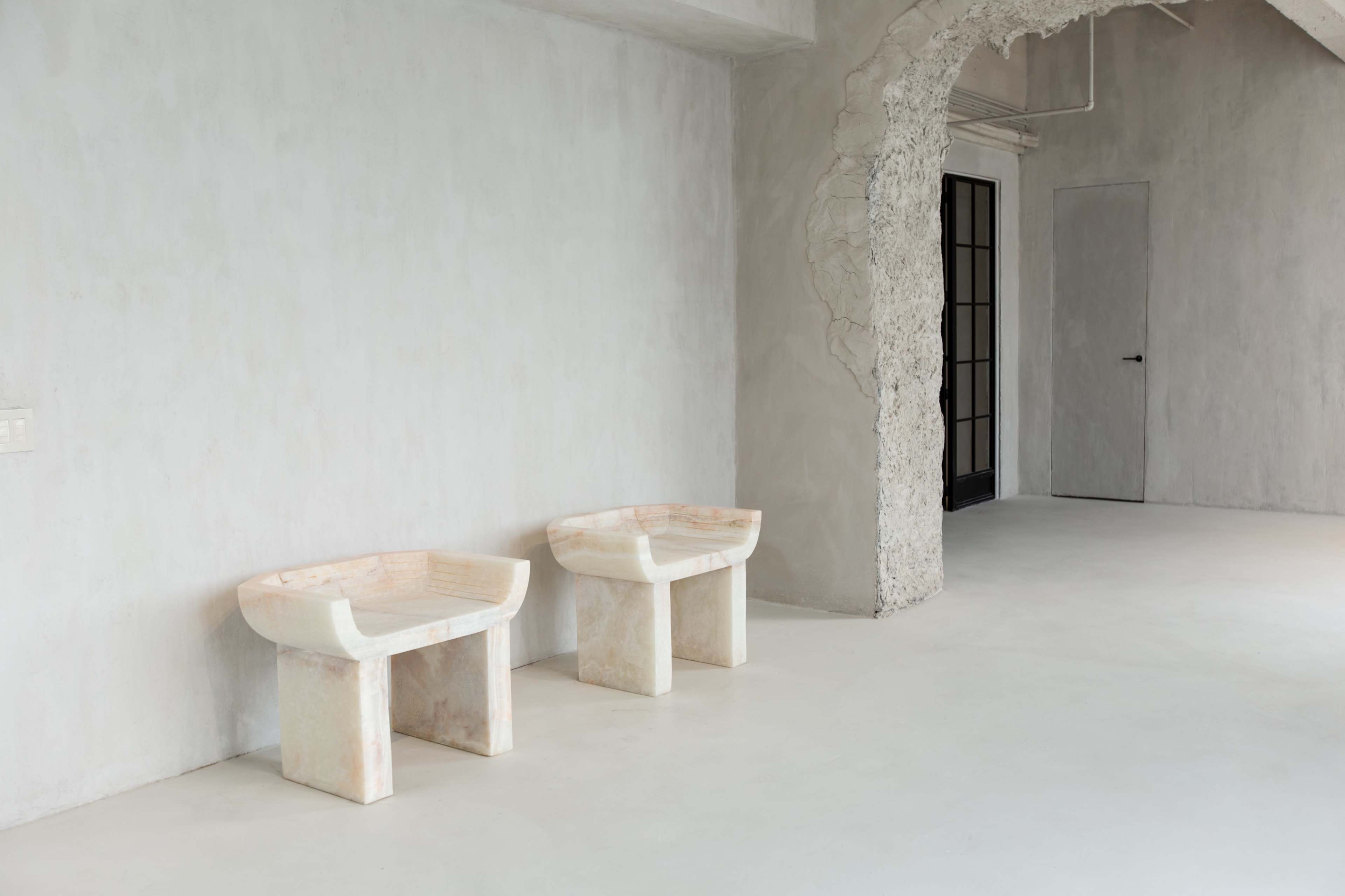 The image features two marble side tables positioned against a textured gray wall in a spacious and minimalist interior.