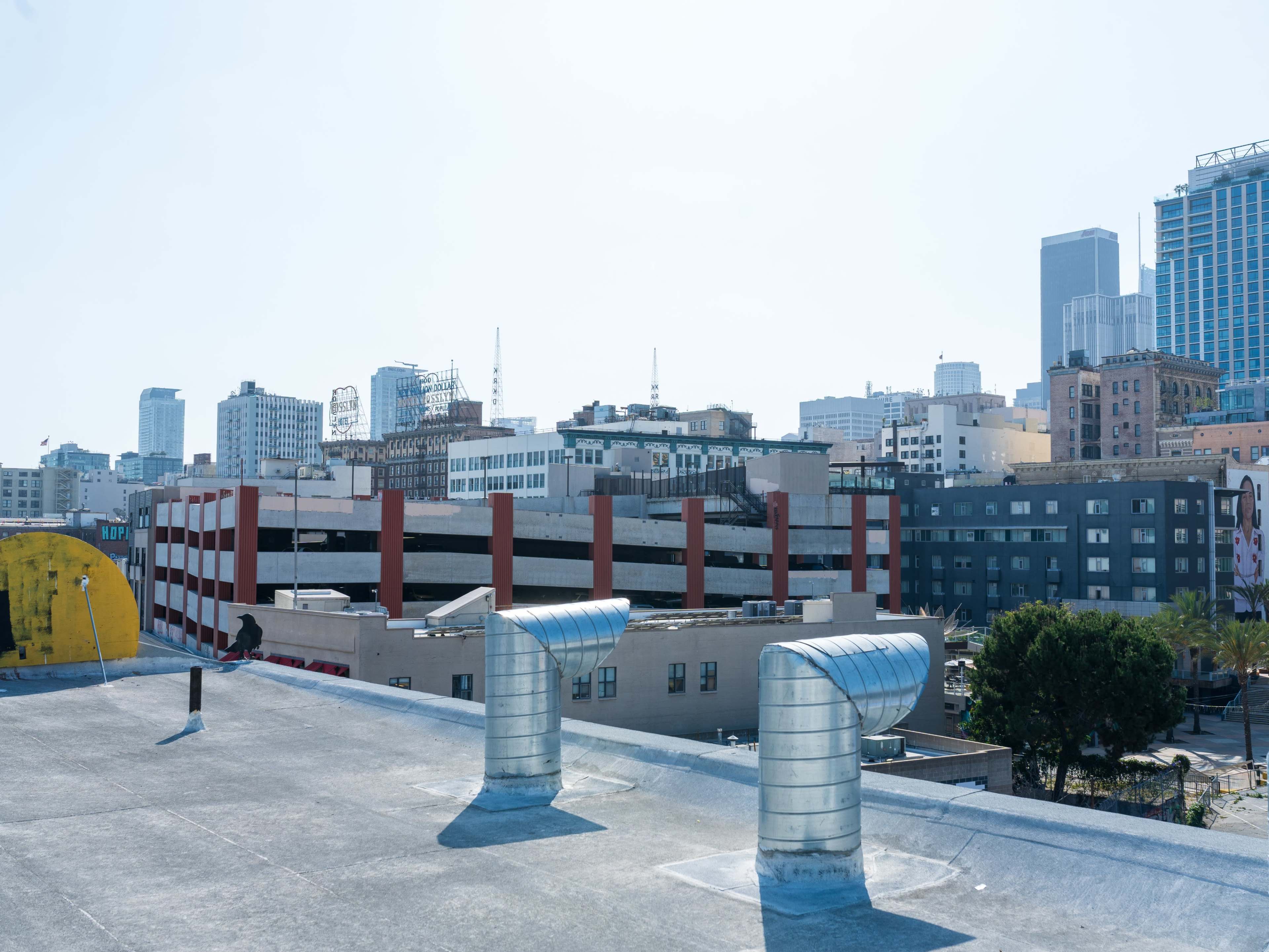 The image shows a rooftop view of a cityscape with various buildings, including a parking structure and high-rise skyscrapers in the background.