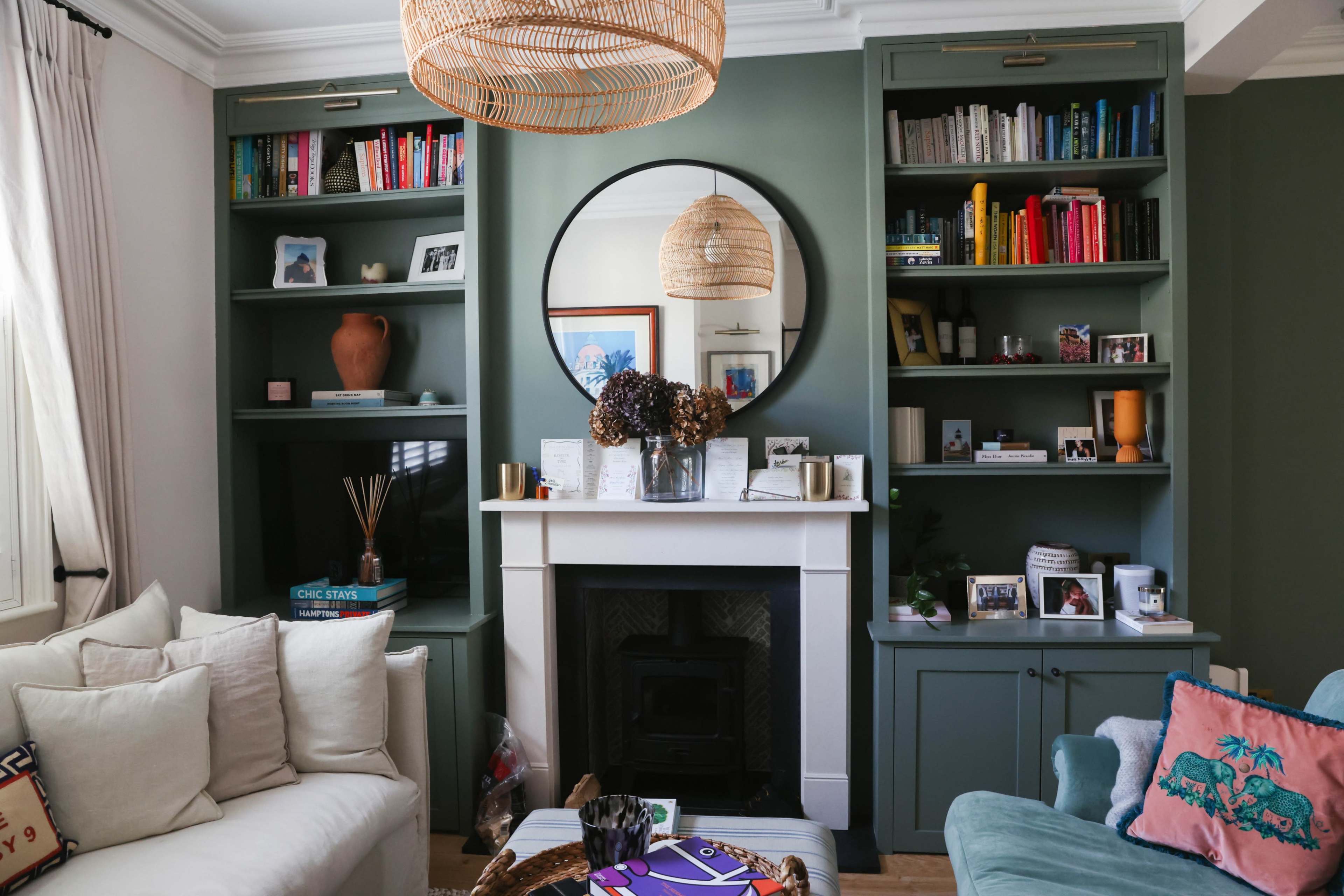 The image shows a well-decorated living room featuring a circular mirror above a mantel, flanked by built-in shelves filled with books and decorative items.