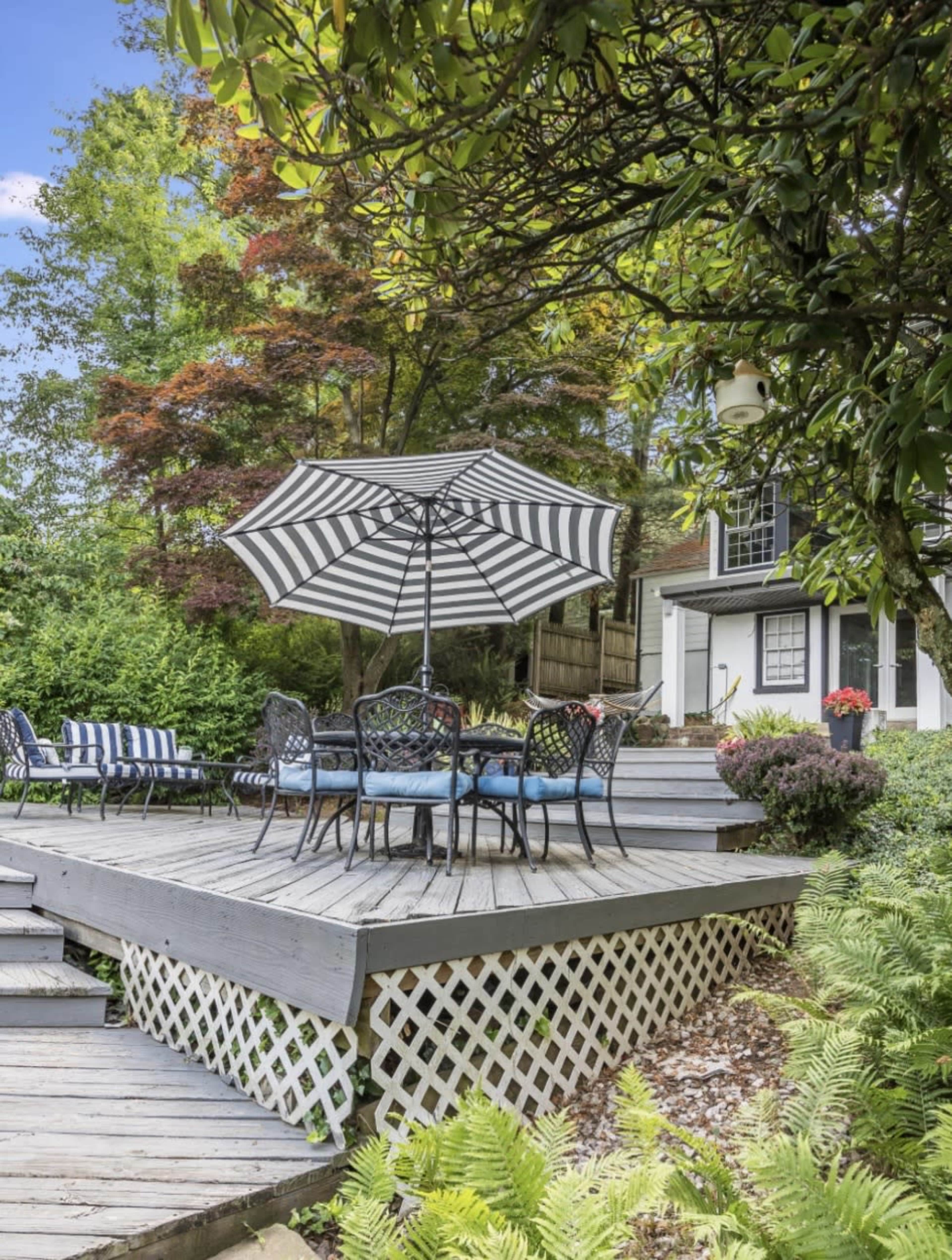A deck with a striped umbrella and seating area is surrounded by greenery and plants.