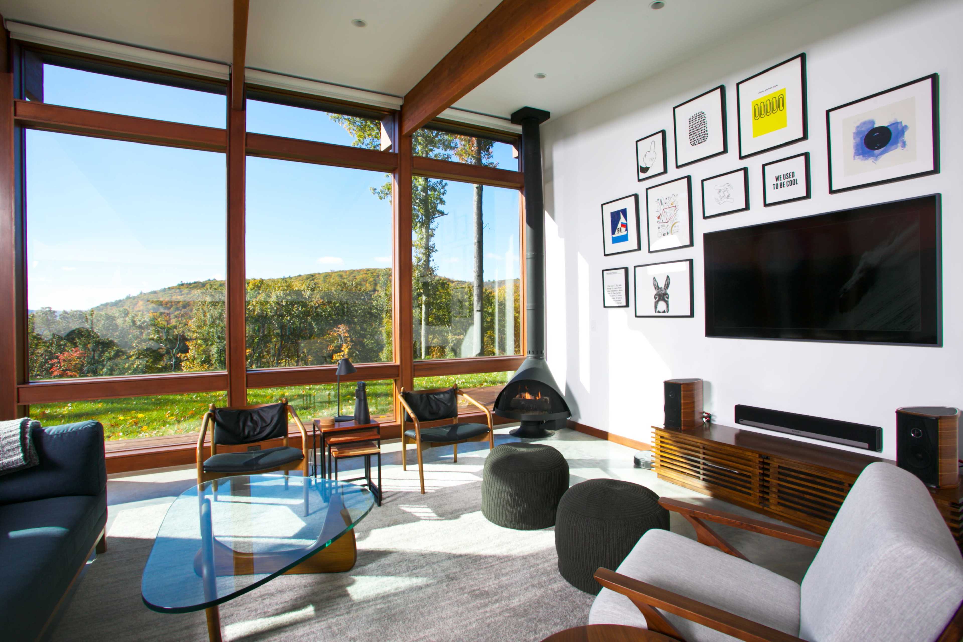 A modern living room features large windows with a view of a green landscape, a wall adorned with framed artwork, and contemporary furniture arrangements.