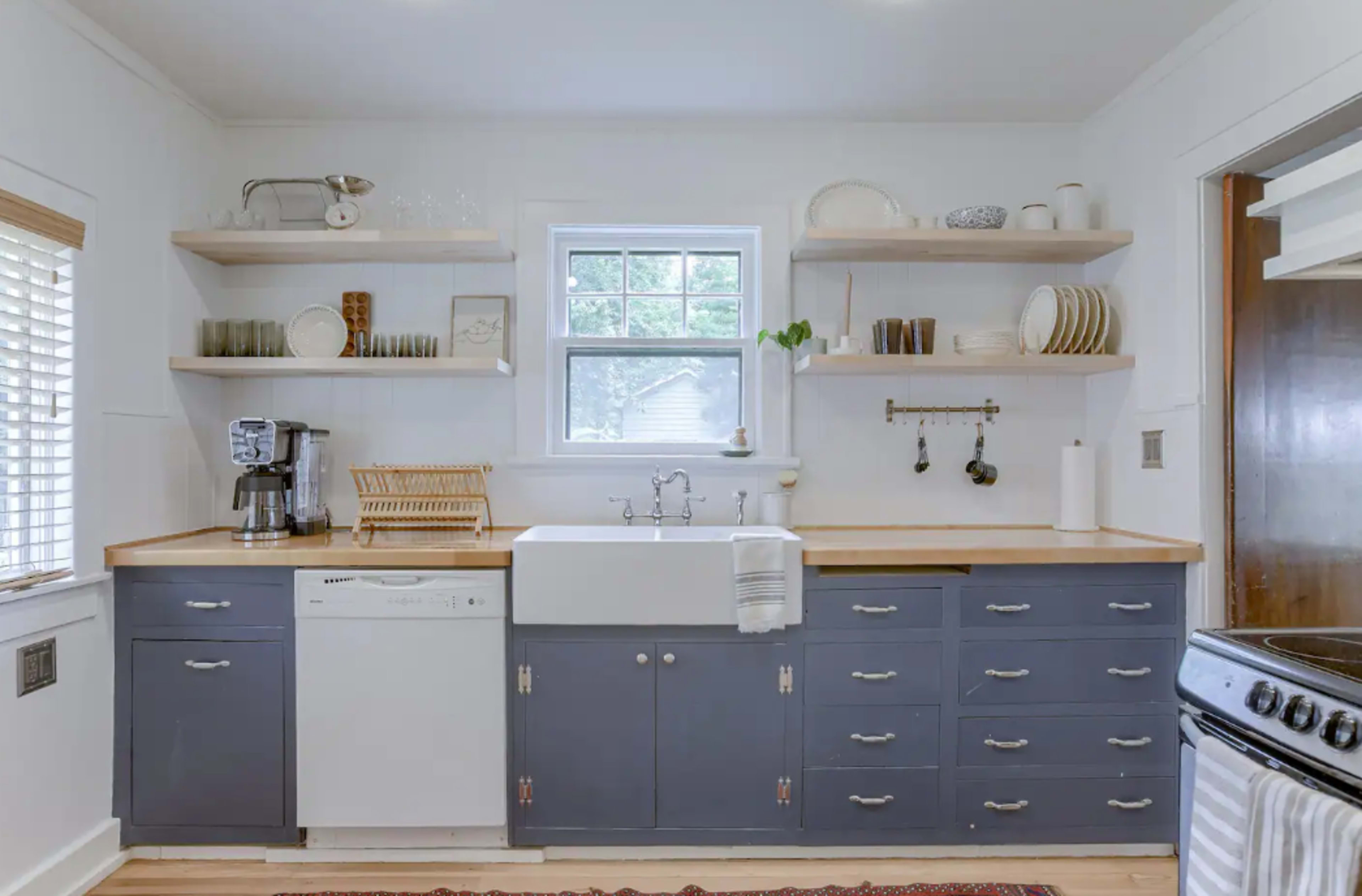 A modern kitchen with a farmhouse sink, open shelving displaying dishes, and a combination of white and navy blue cabinetry.