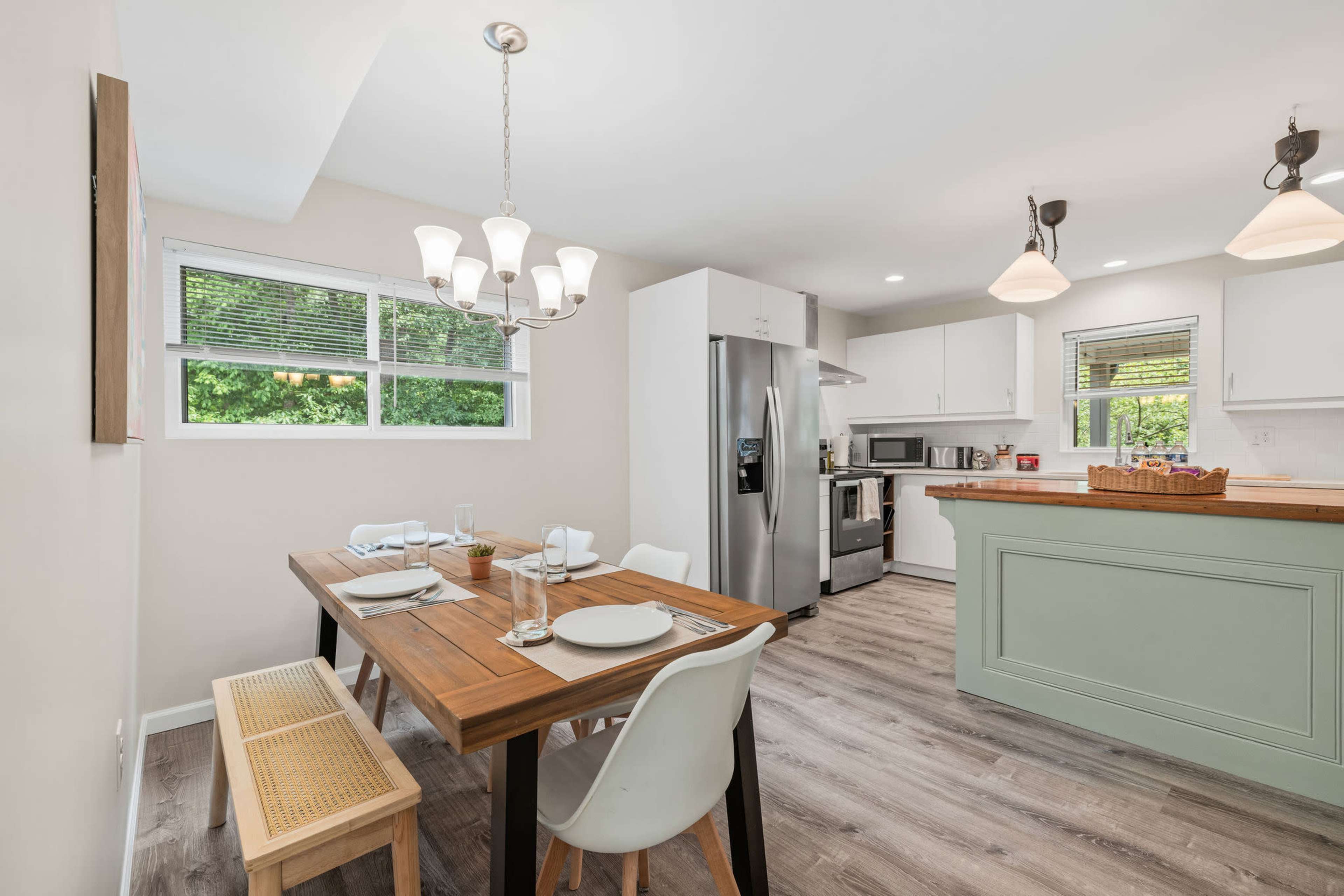 The image shows a modern kitchen and dining area featuring a wooden dining table, white chairs, and stainless steel appliances.