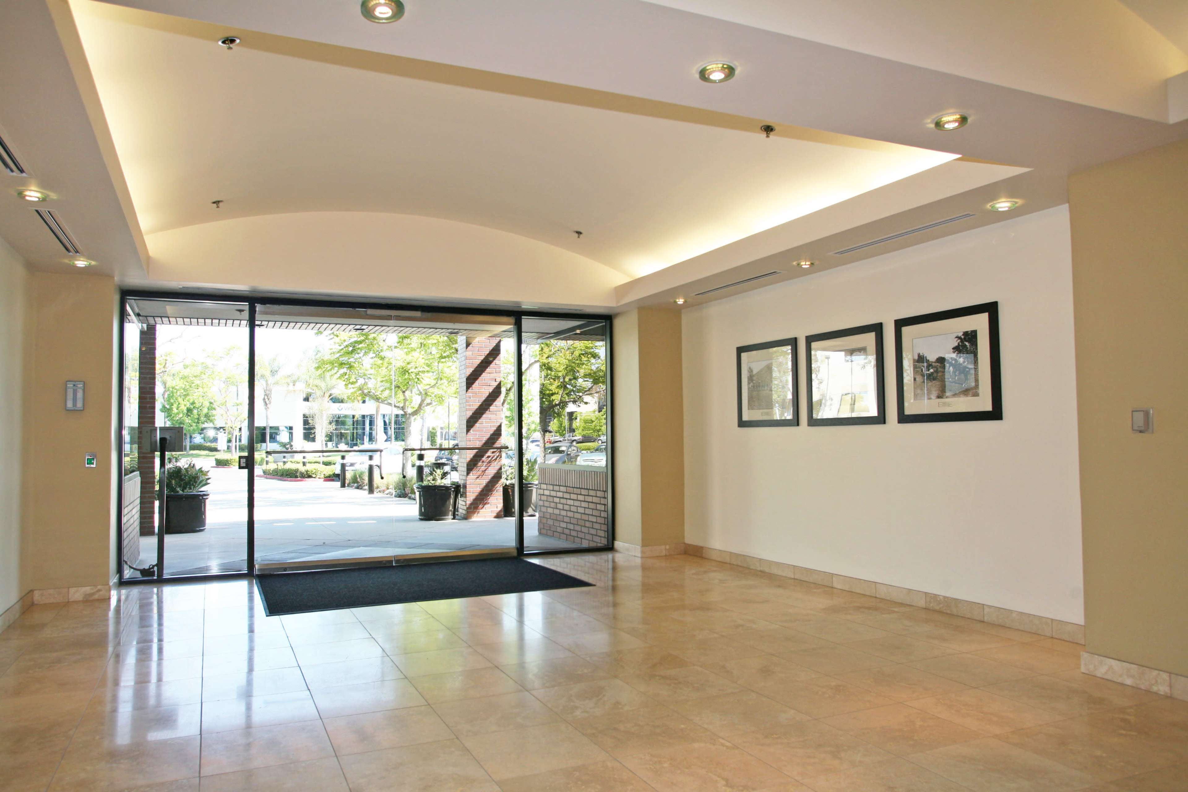 The image shows a spacious lobby with tile flooring, large glass doors leading outside, and framed artwork on the wall.