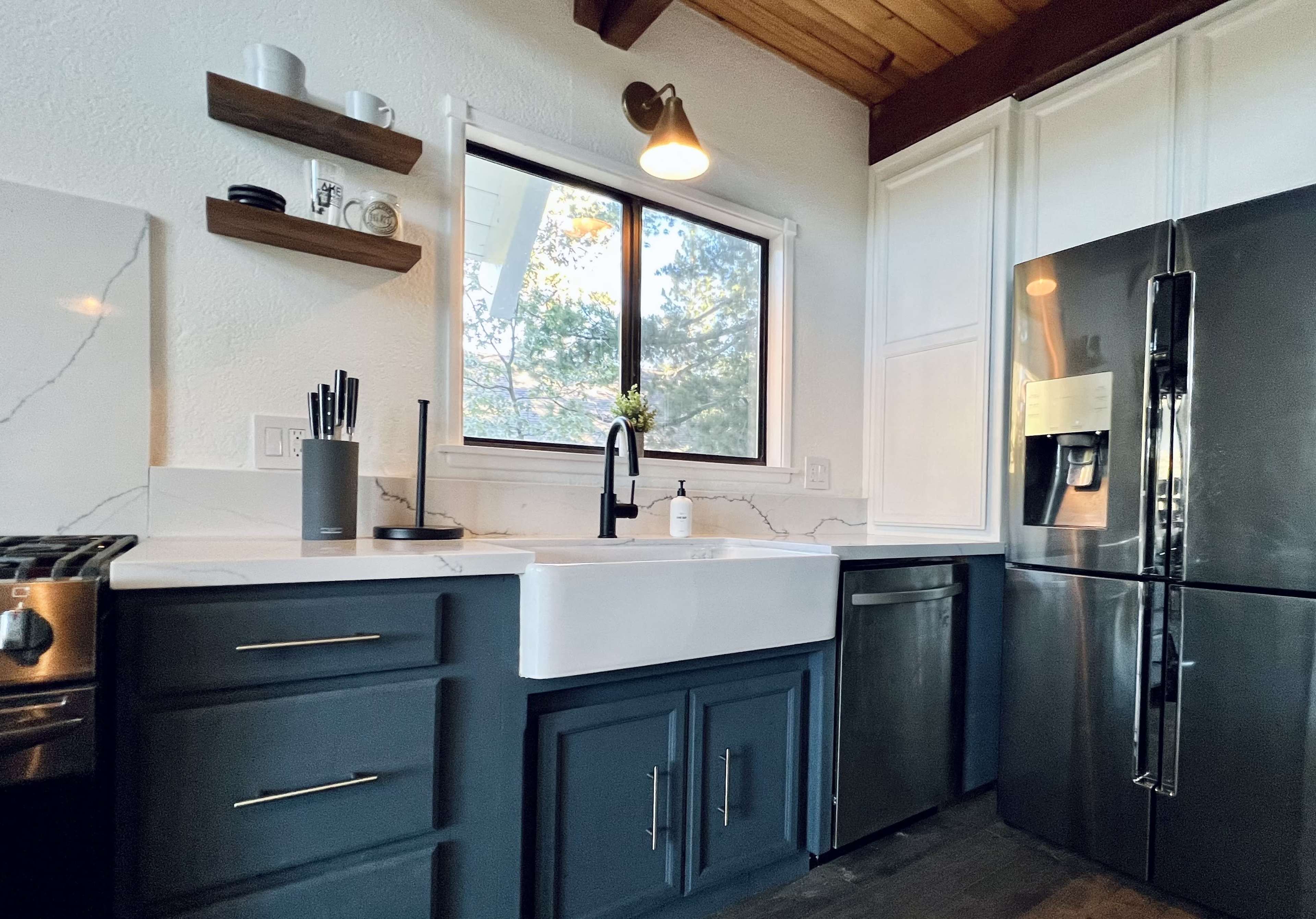 The image shows a modern kitchen featuring a farmhouse sink, dark cabinetry, and stainless steel appliances.