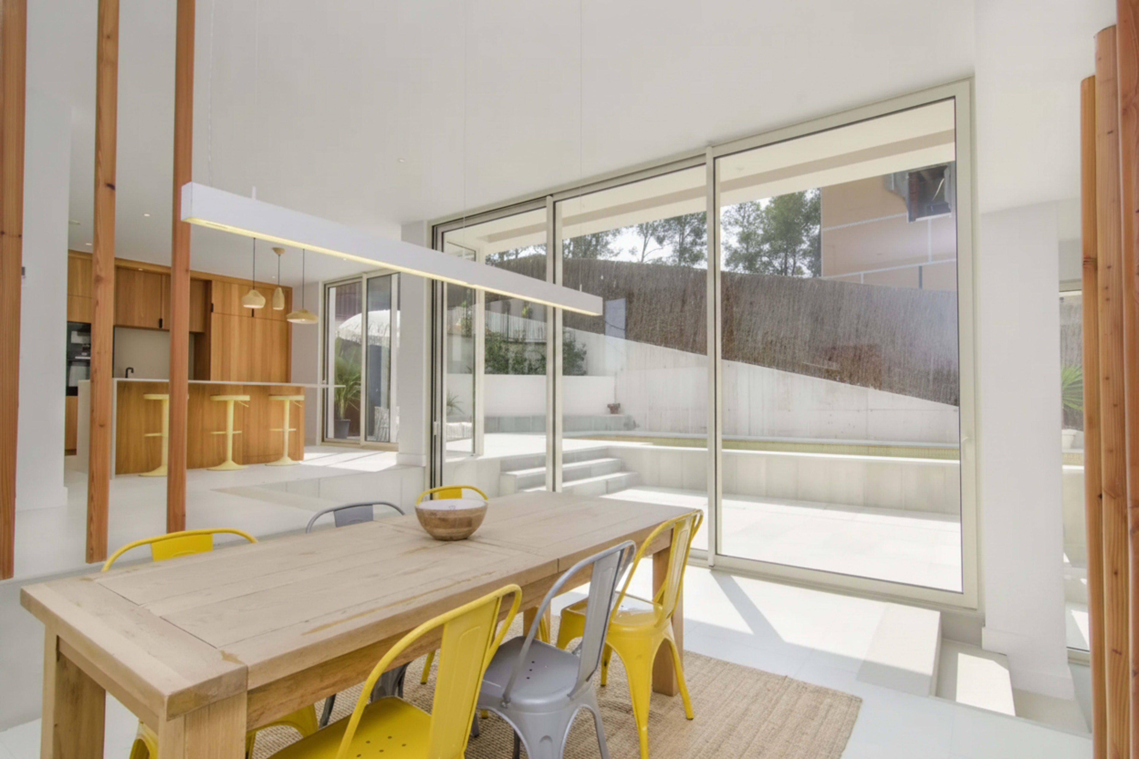 A bright dining area features a wooden table surrounded by colorful metal chairs and large glass doors leading to an outdoor space.