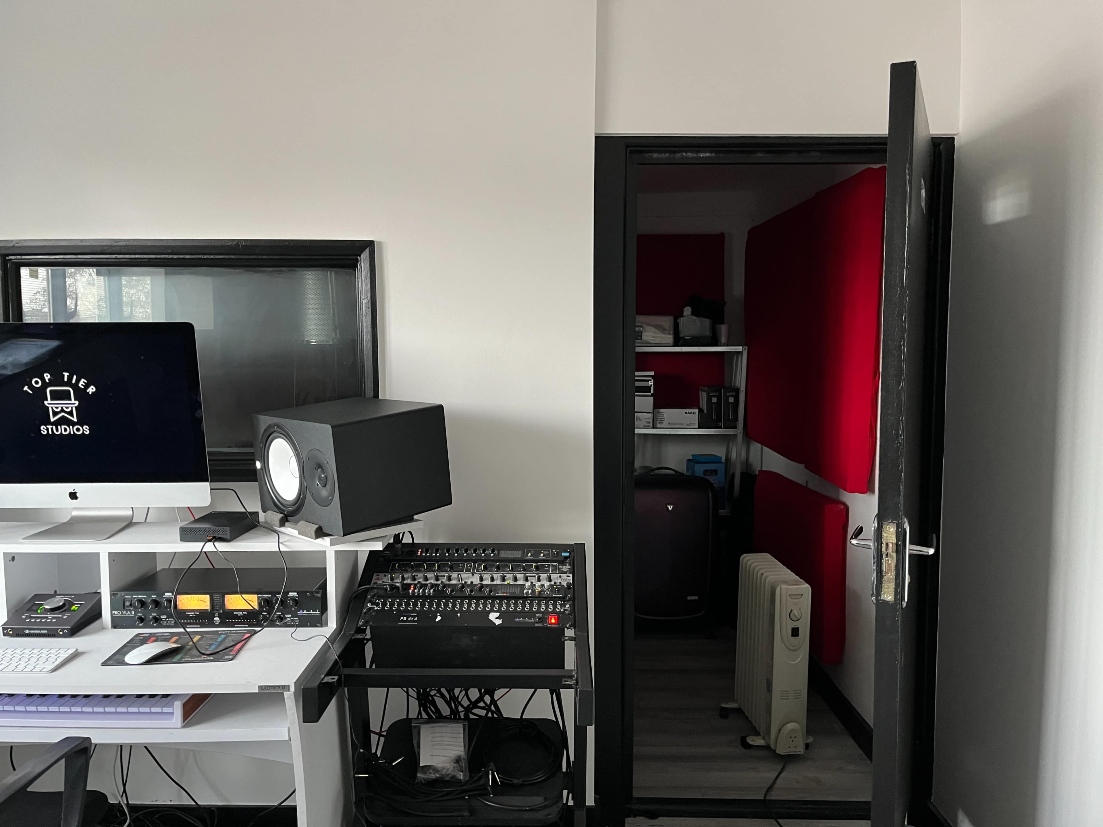 A modern recording studio features a computer setup, audio equipment, and a door leading to a soundproof room.