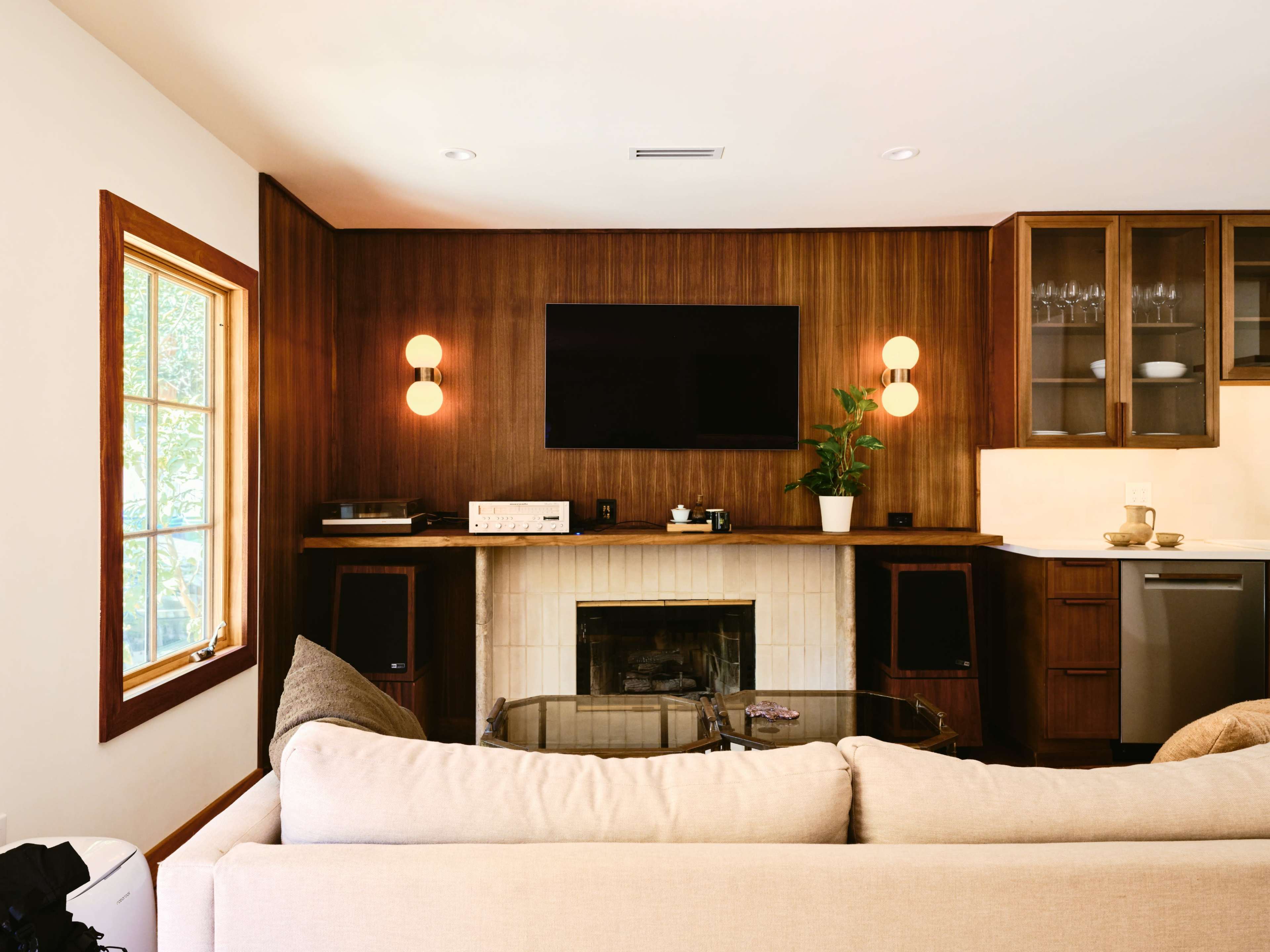 A modern living room features a sofa facing a wall with a flat-screen TV, a fireplace, and built-in cabinetry with decorative lighting.