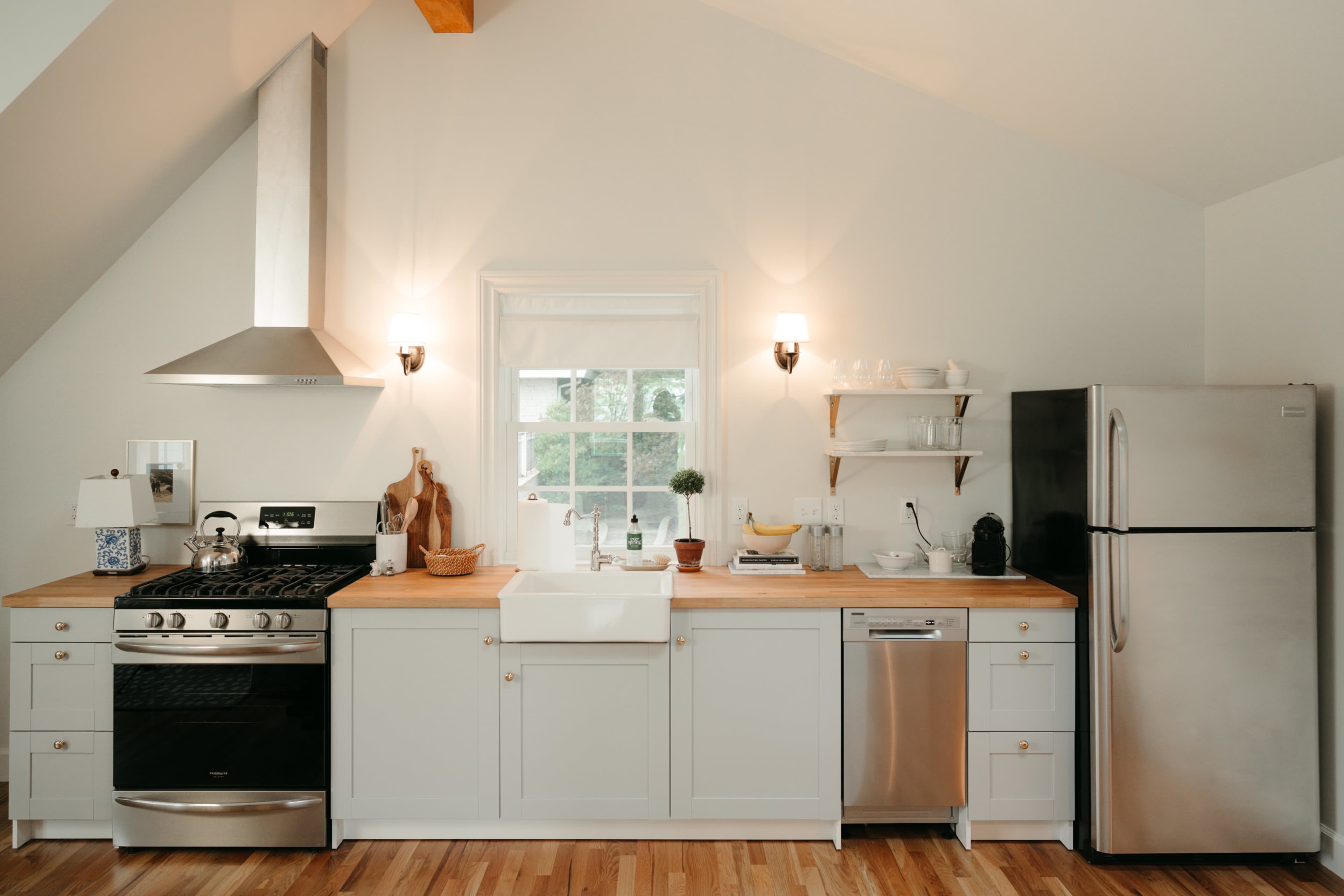 A modern kitchen features white cabinets, a stainless steel refrigerator, and a farmhouse sink beneath a window.