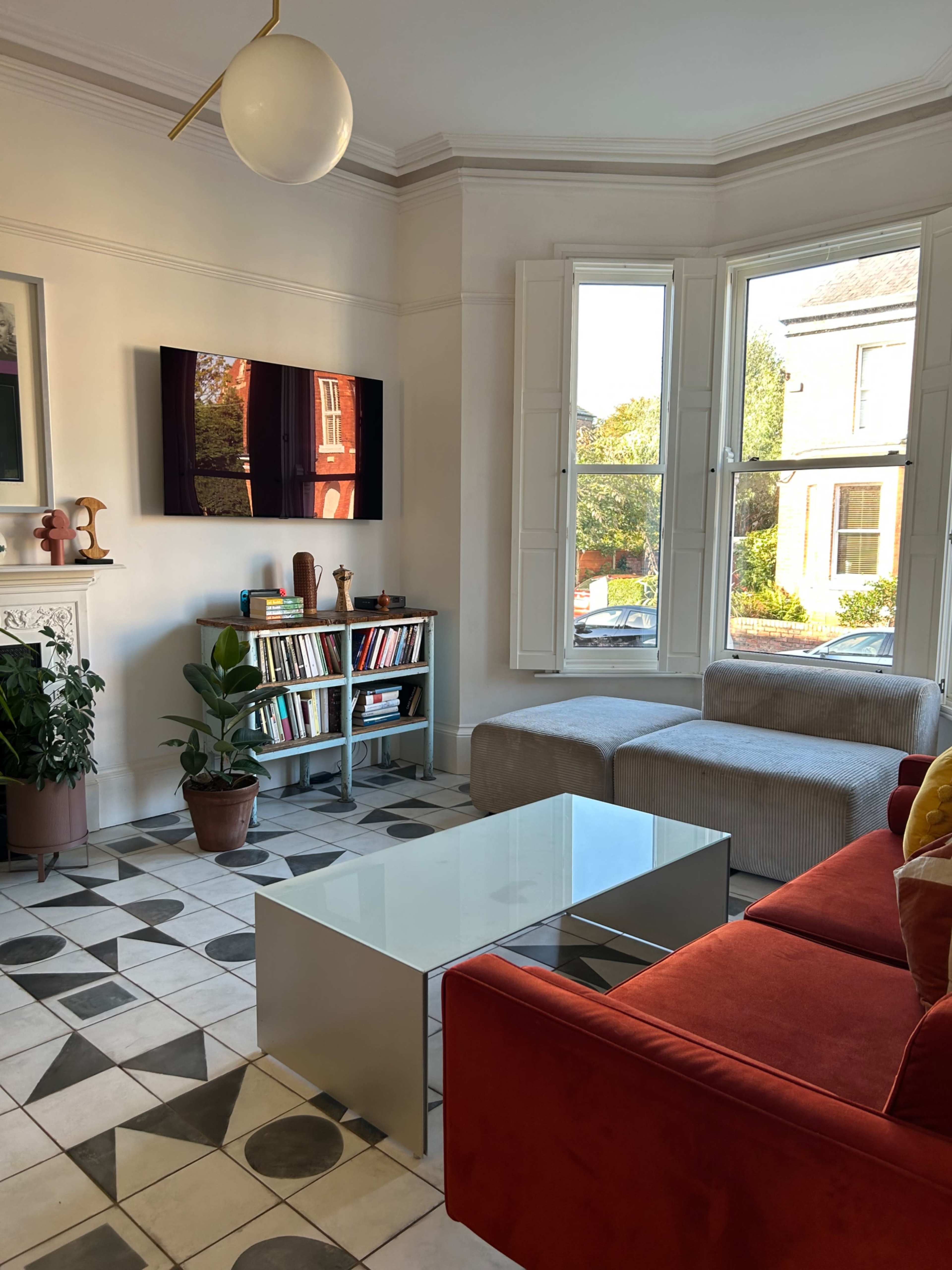 A modern living room with a red sofa, a glass coffee table, and a bookshelf next to large windows that let in natural light.