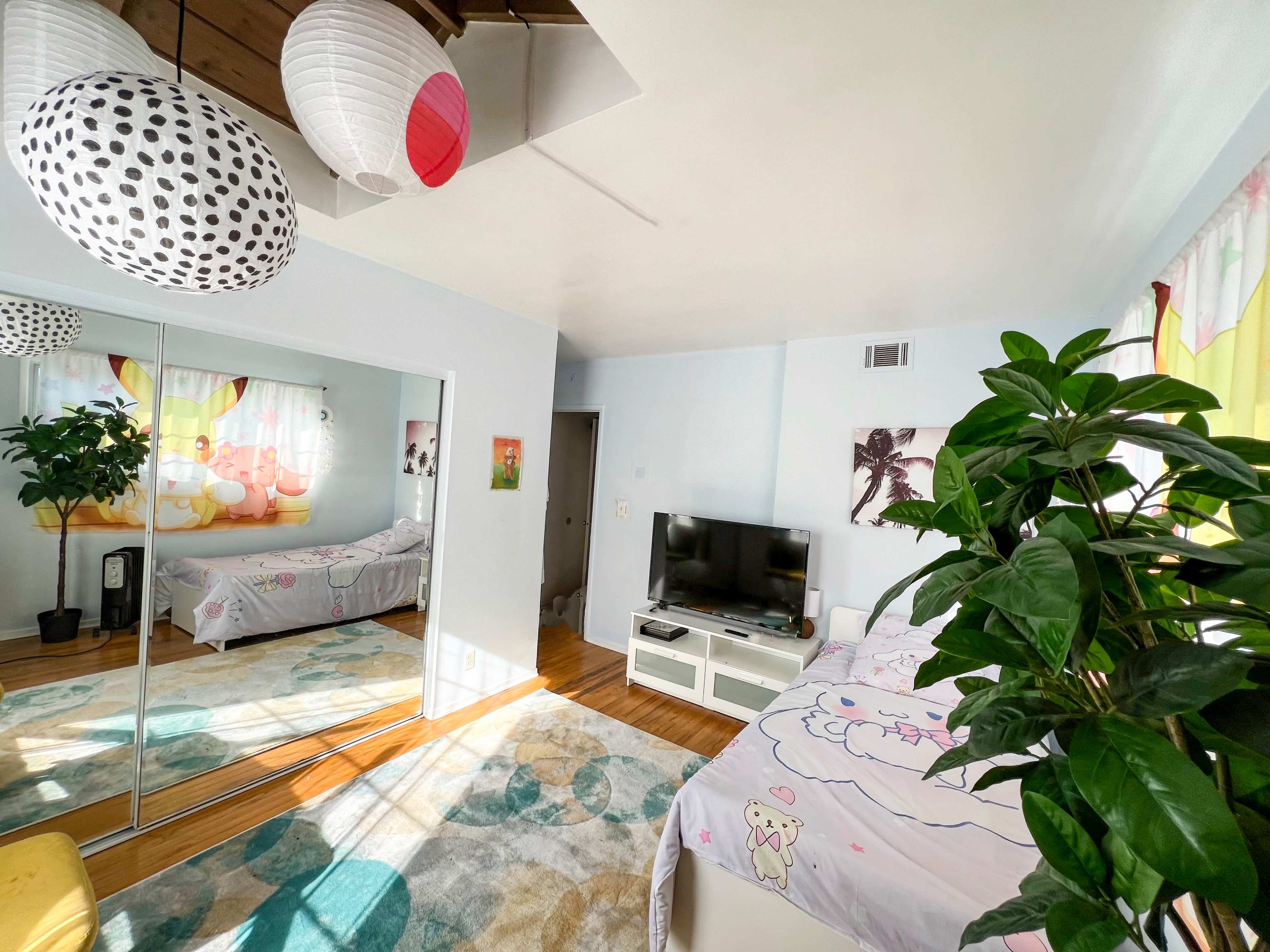 The image shows a room with a bed, television, a large mirror, and decorative paper lanterns hanging from the ceiling.