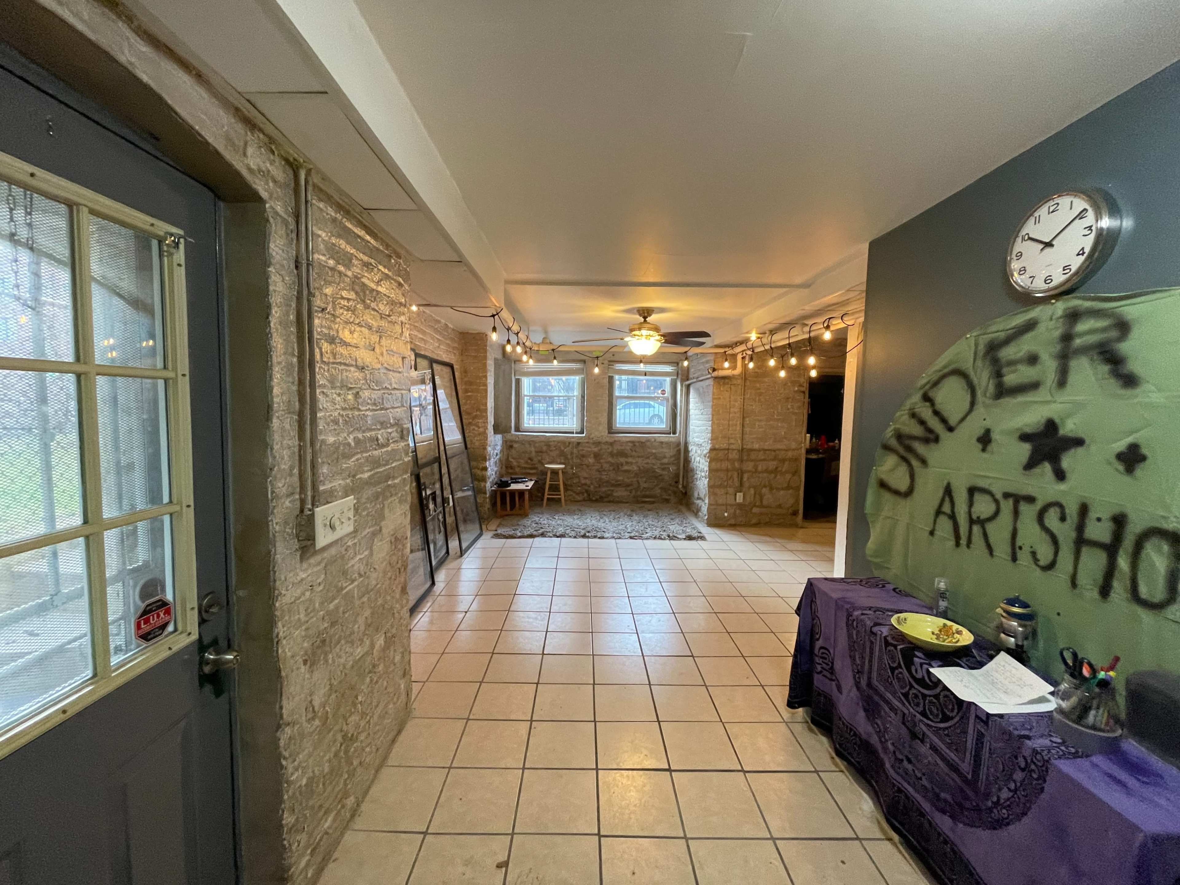 A spacious room with stone walls, tiled floors, string lights, and a table set up with various items.