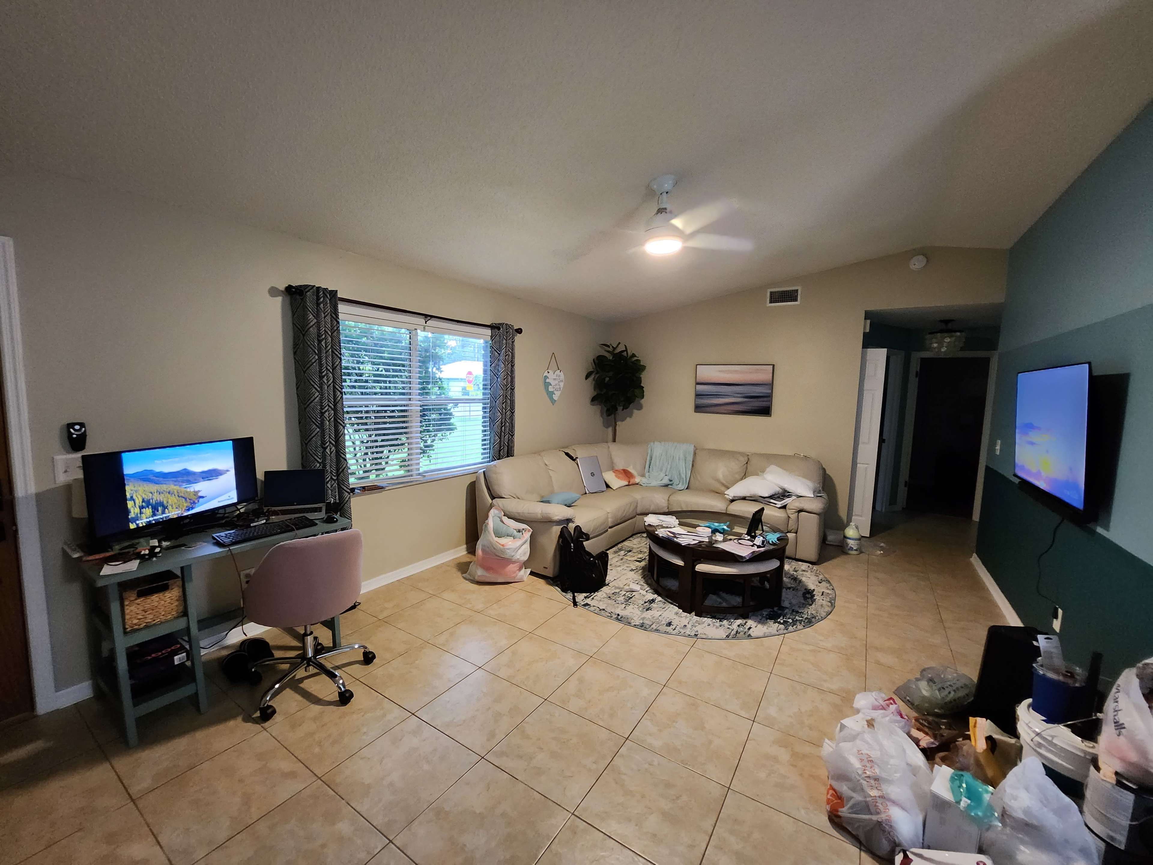 A living room with a sofa, two computers on a desk, and bags of items scattered on the floor.
