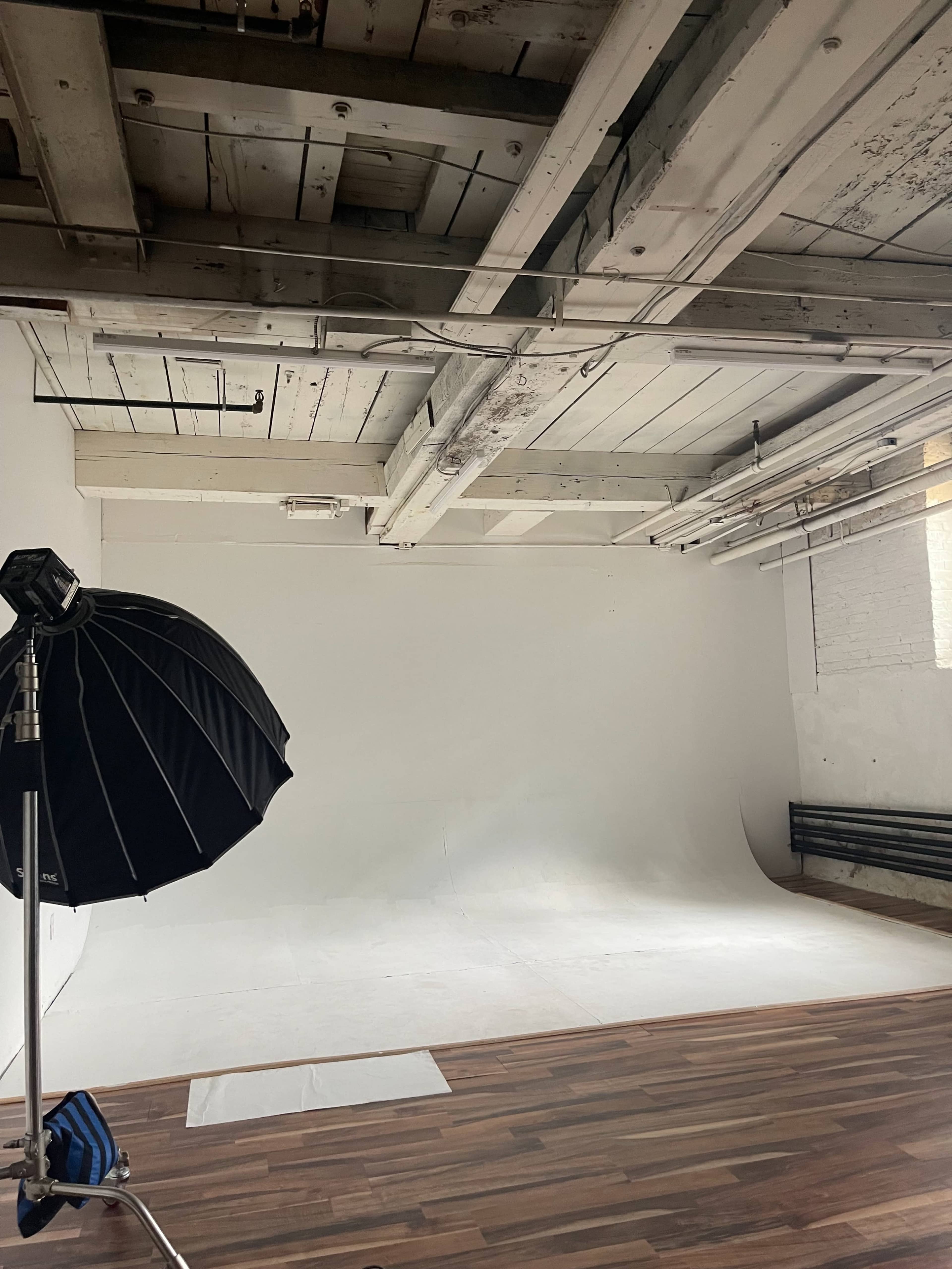 A photography studio with a large softbox on a stand, a white backdrop, and wooden flooring.