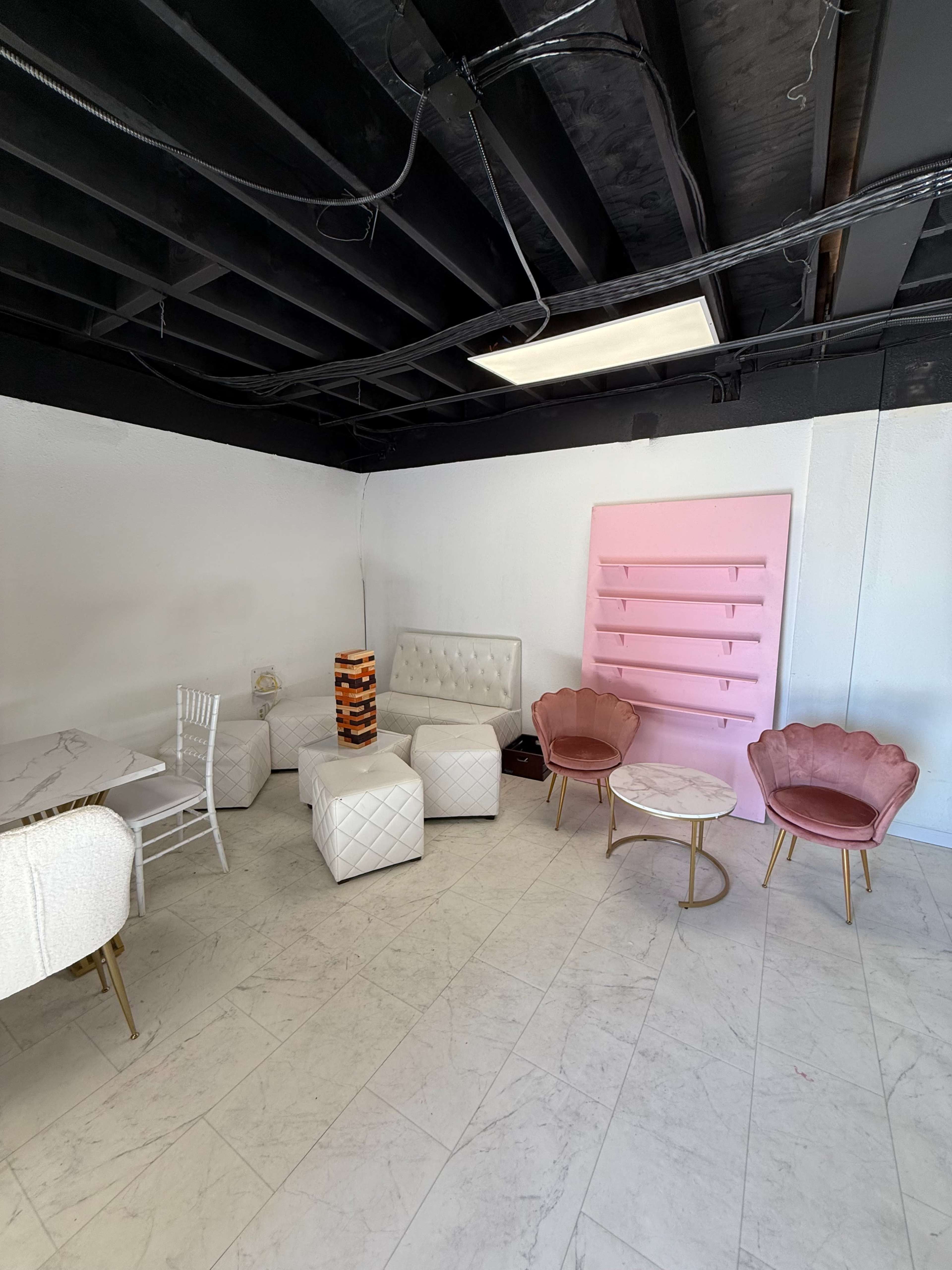 The image shows a modern, minimalist seating area with white furniture, pink decorative elements, and a light-colored floor.