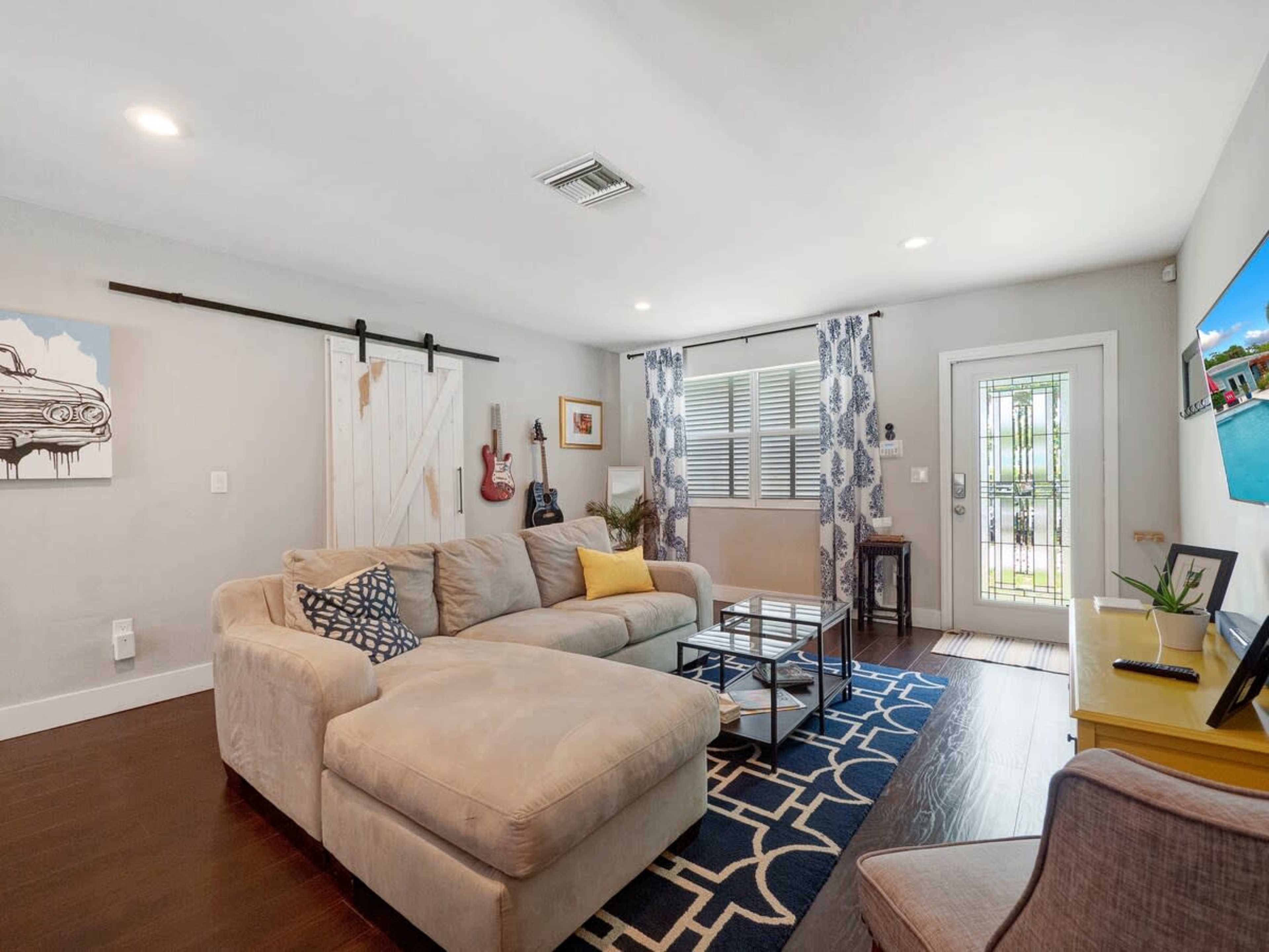 A spacious living room features a sectional sofa, a glass coffee table, and a doorway leading to an outdoor area.