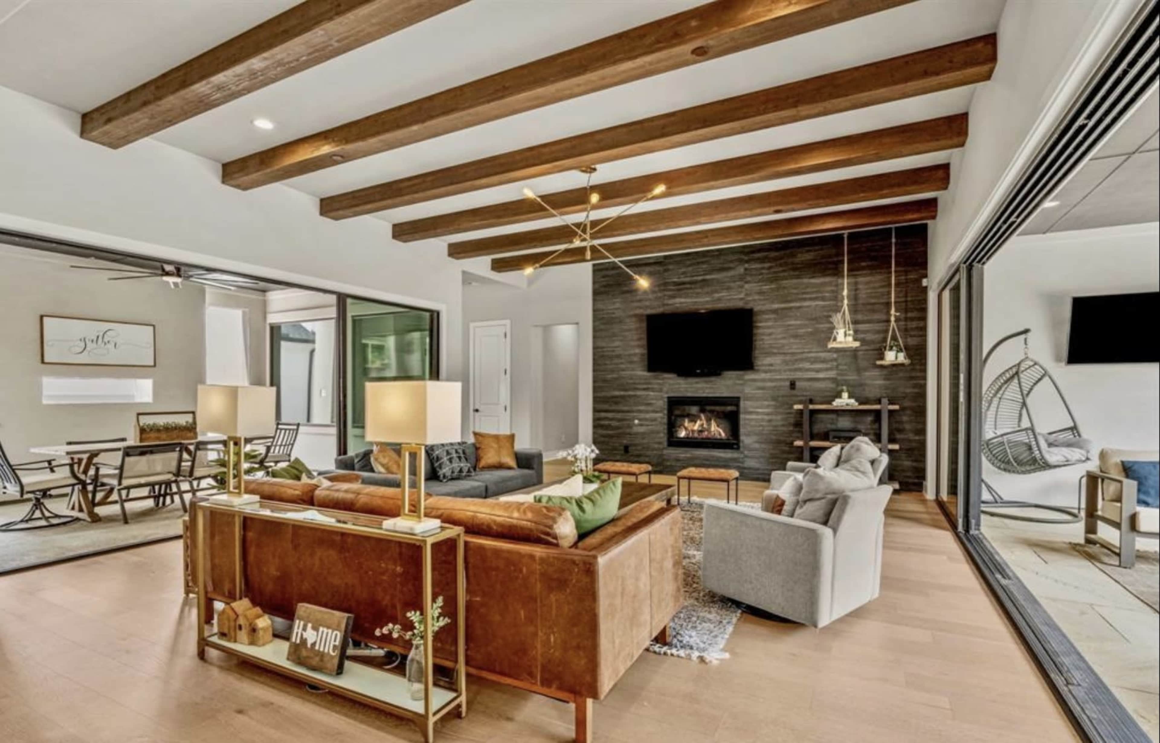 The image shows a modern living room with wooden beams, a fireplace, and a mix of seating arrangements including leather and fabric sofas.