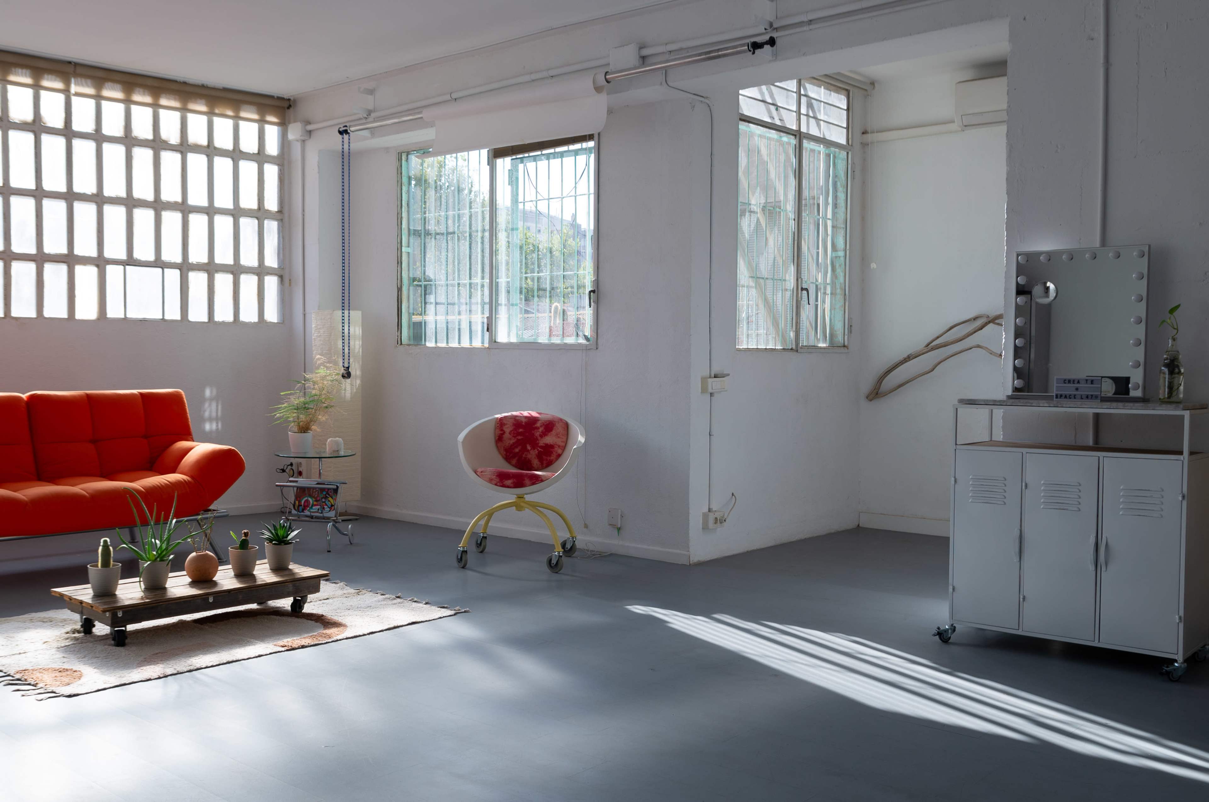 A bright, spacious room featuring a red sofa, a decorative wooden table, large windows, and a vanity cabinet.