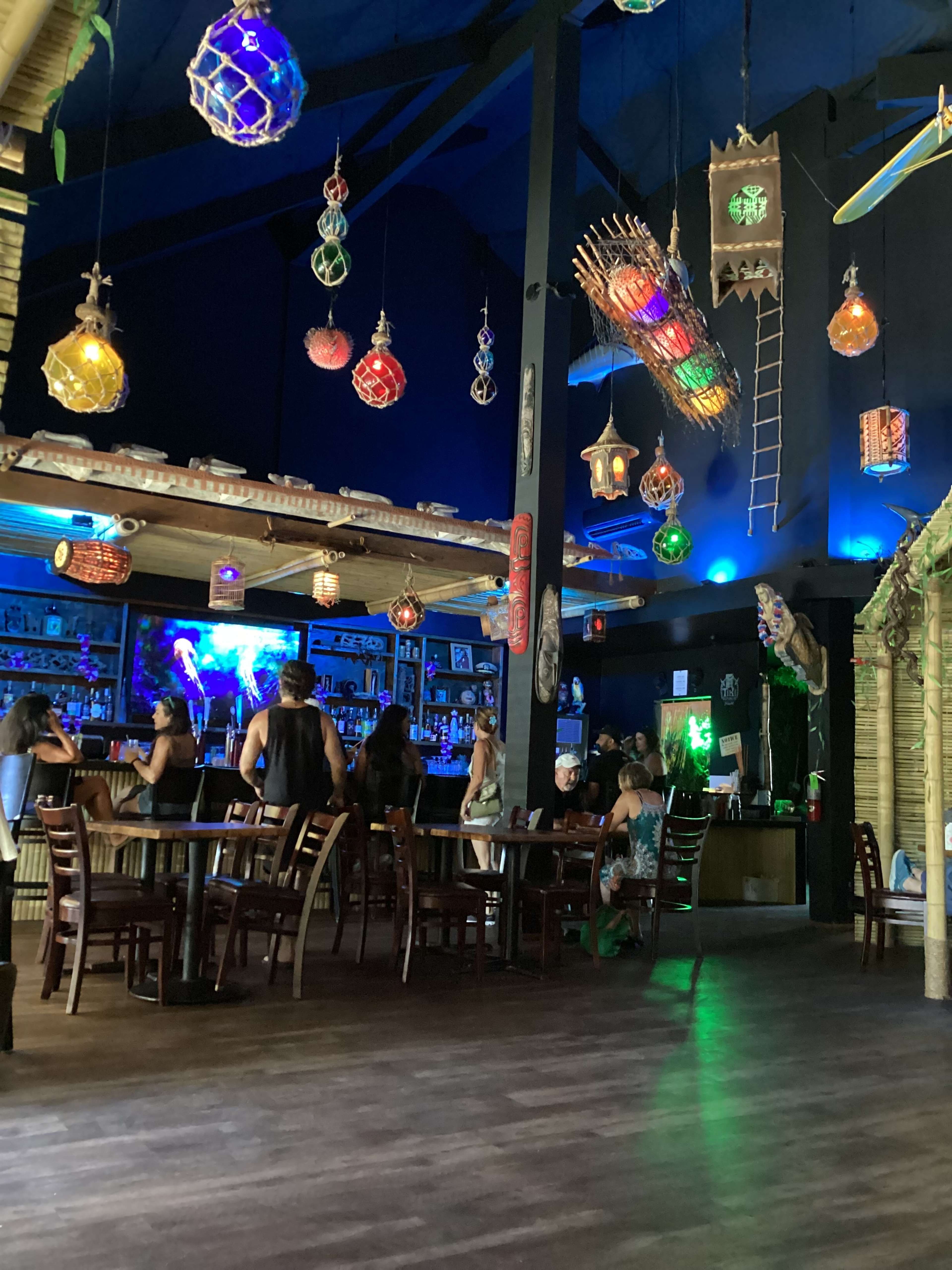 The image shows a vibrant bar scene with colorful hanging lanterns and patrons seated at tables, surrounded by a lively atmosphere.