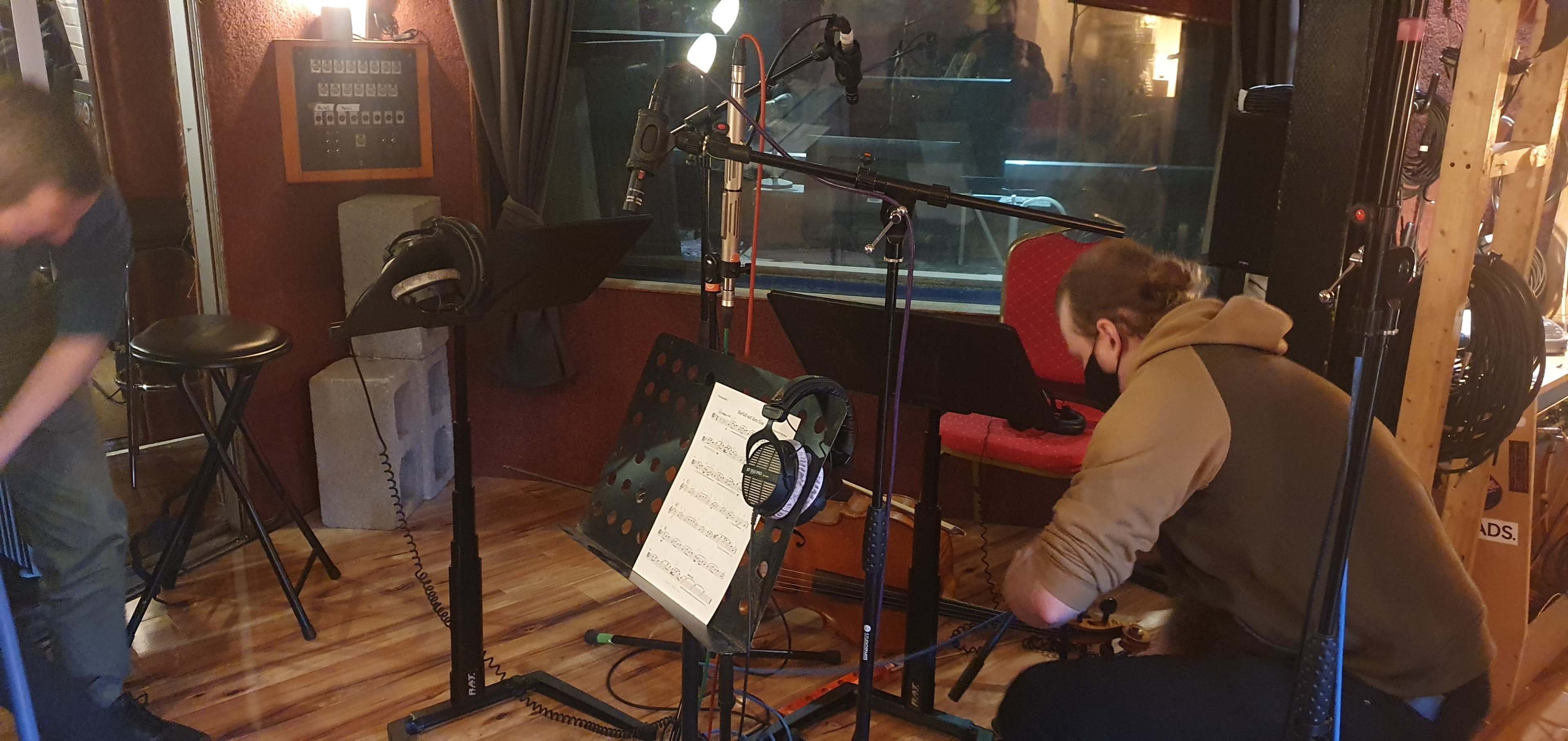 Two individuals are setting up equipment in a recording studio, surrounded by microphones and music stands.