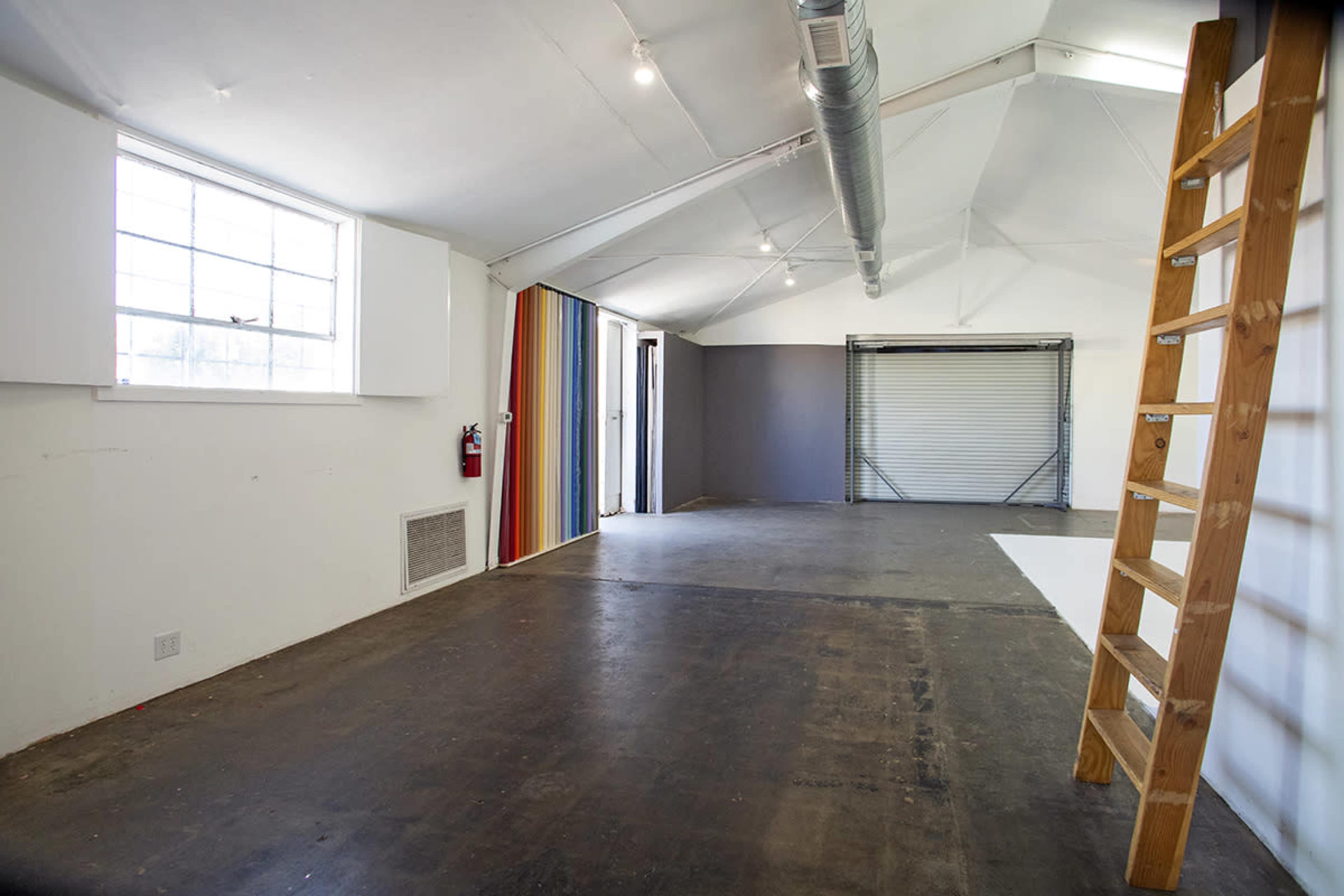 A spacious room with a ladder on the right side, a large window, and colorful striped wall panels.