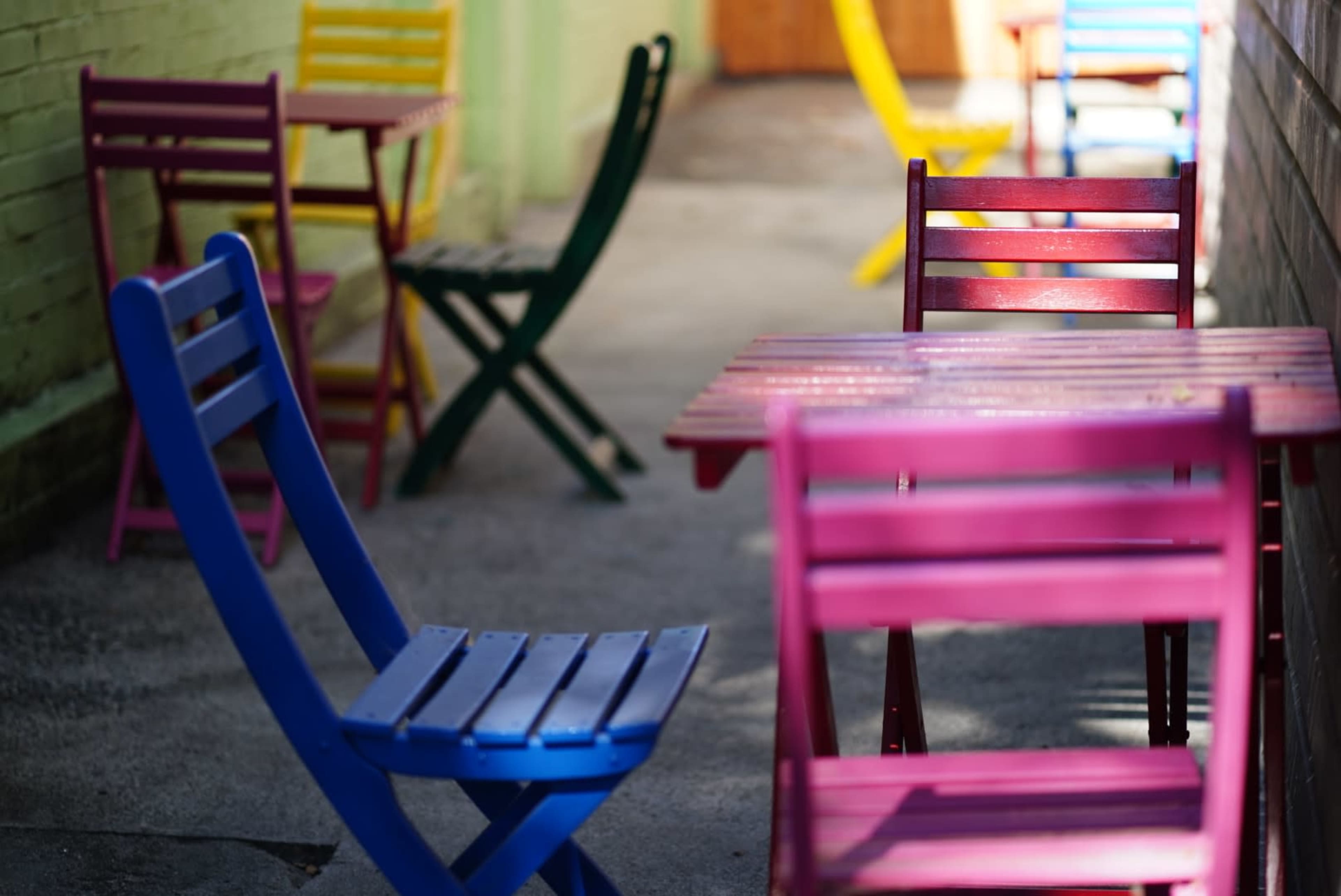 Colorful folding chairs and tables are arranged in a narrow outdoor space.