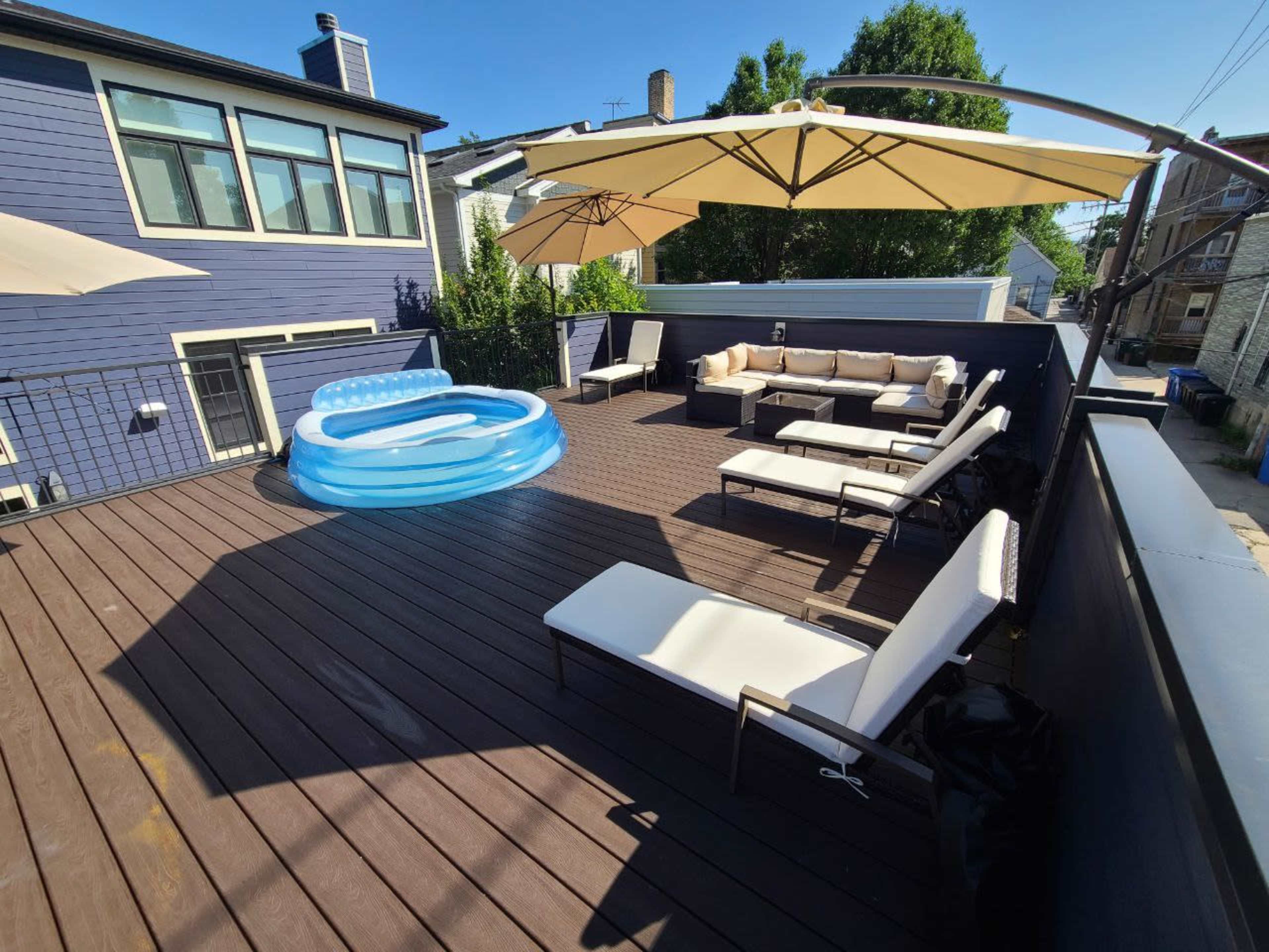 A deck with several lounge chairs, a small inflatable pool, and large umbrellas providing shade.