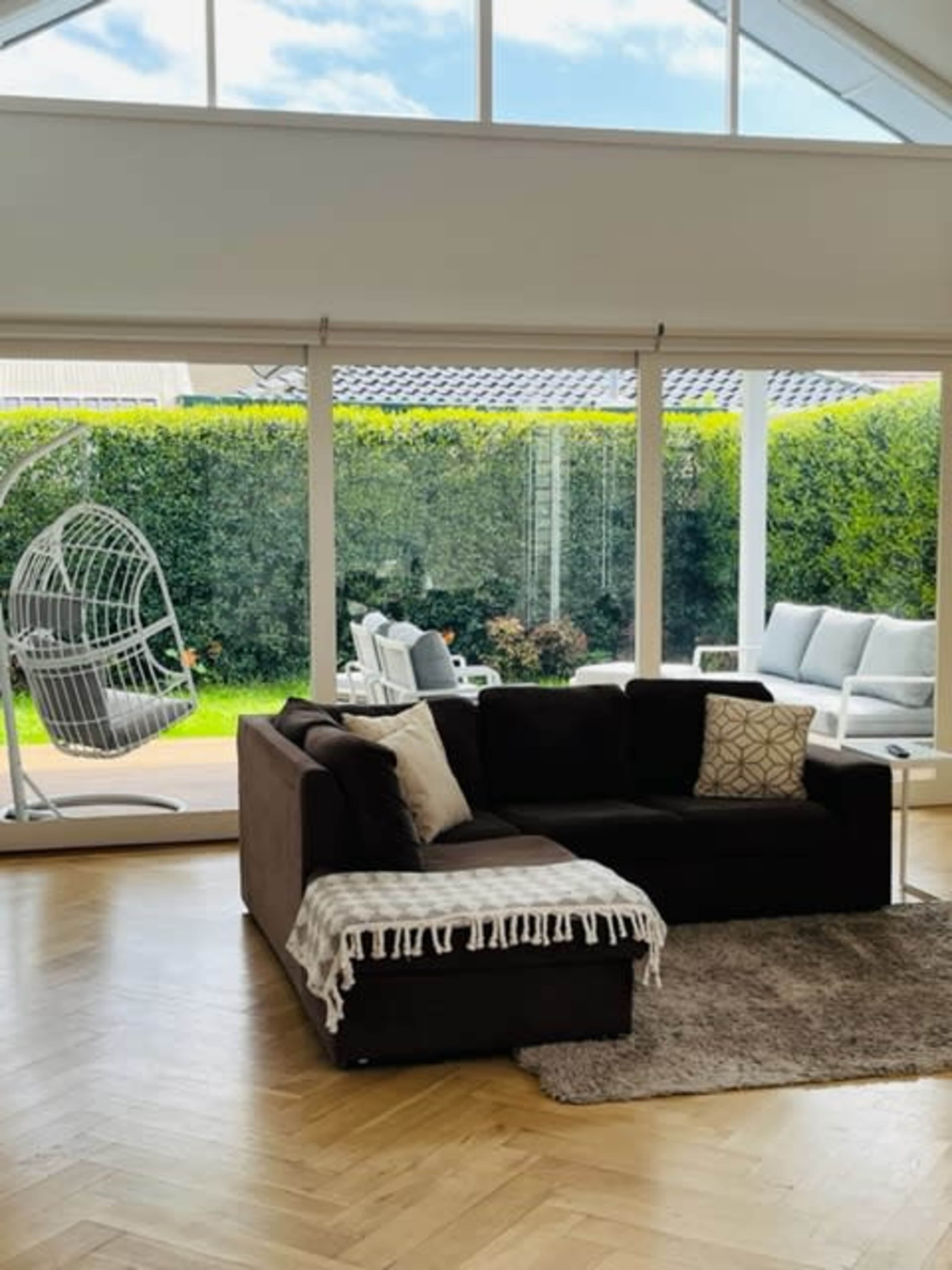 A dark brown sectional sofa with a throw blanket sits in a bright room overlooking a patio with a hanging chair and outdoor seating.
