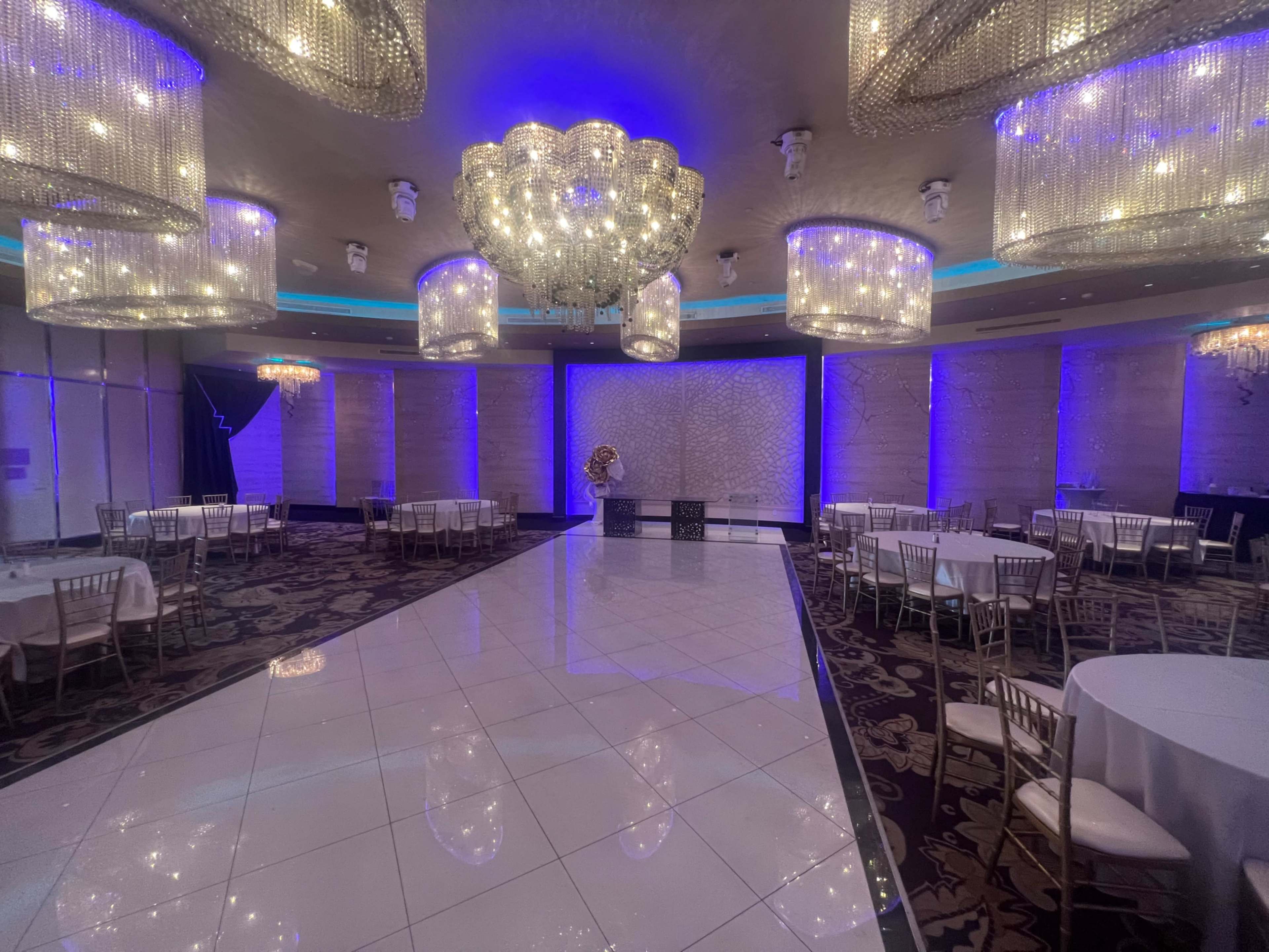 An elegantly designed banquet hall with large crystal chandeliers, a polished white floor, and round tables set up for an event.